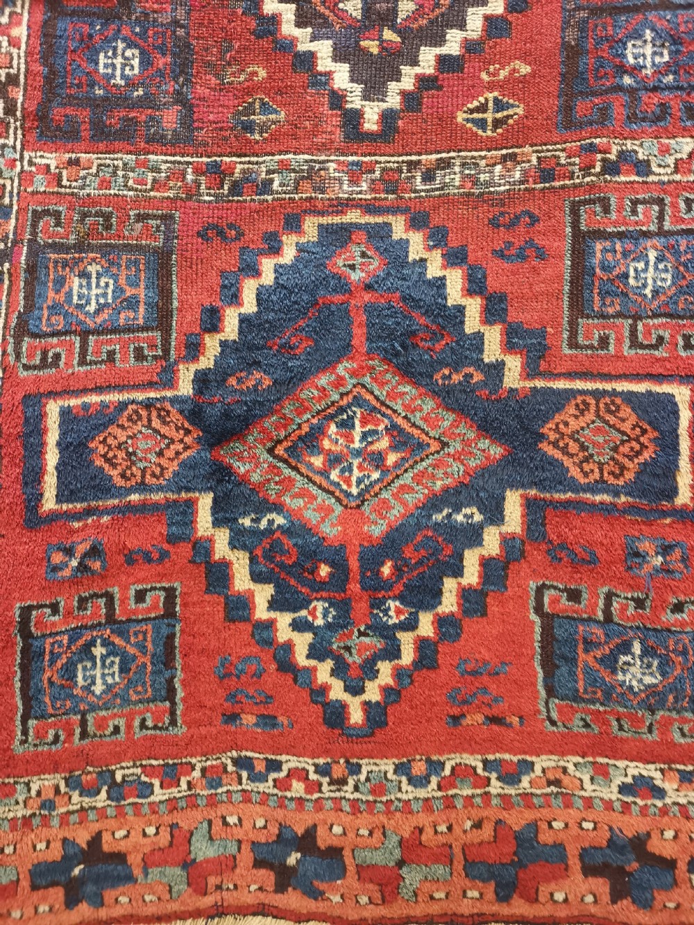 An antique East Anatolian Kurdish wool rug featuring a red ground with three large geometric medallions in indigo blue, framed by intricate tribal borders. View V