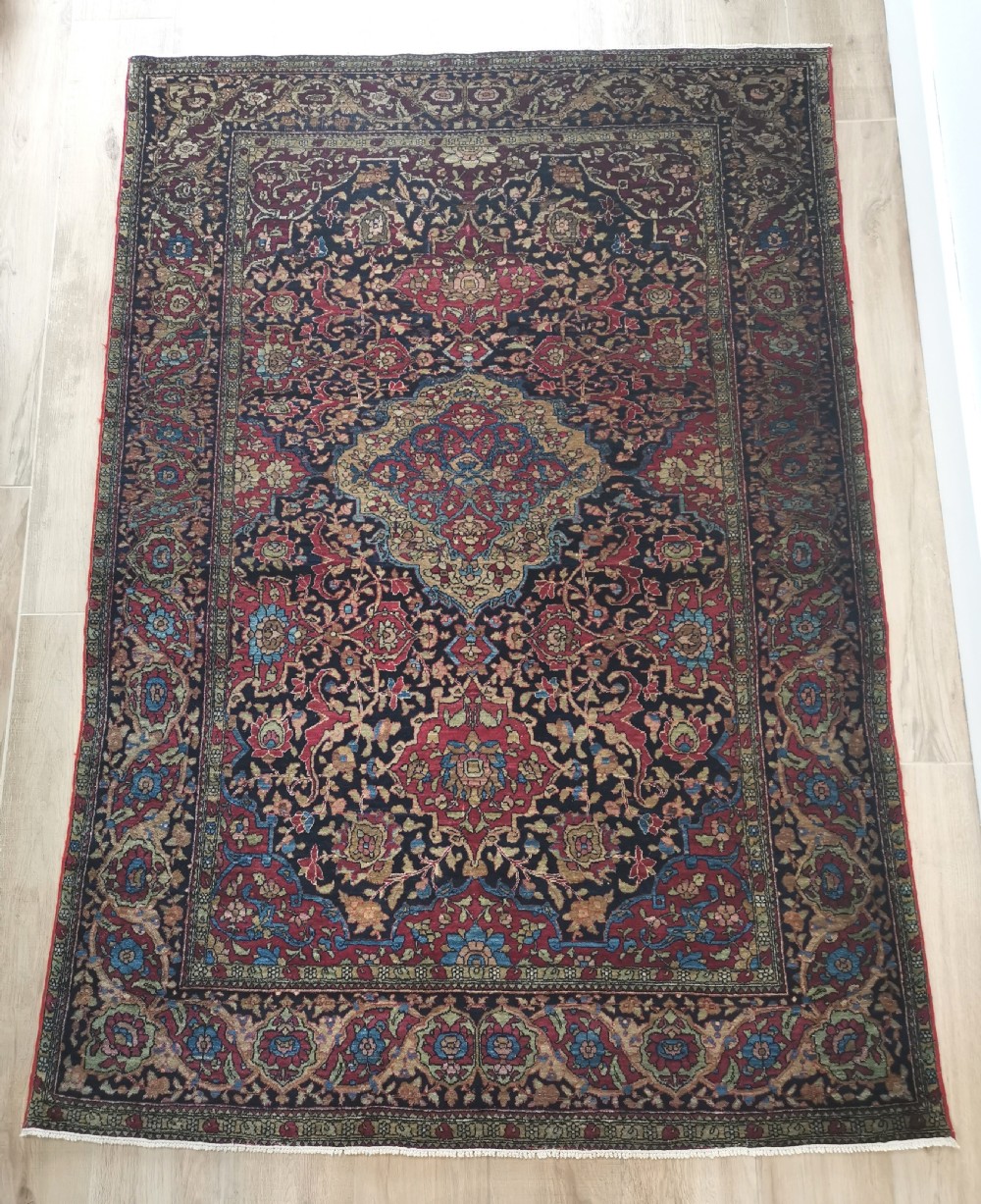 A rectangular hand-knotted Persian Isfahan rug featuring a central medallion with intricate floral arabesques in navy, deep red, and beige tones.
