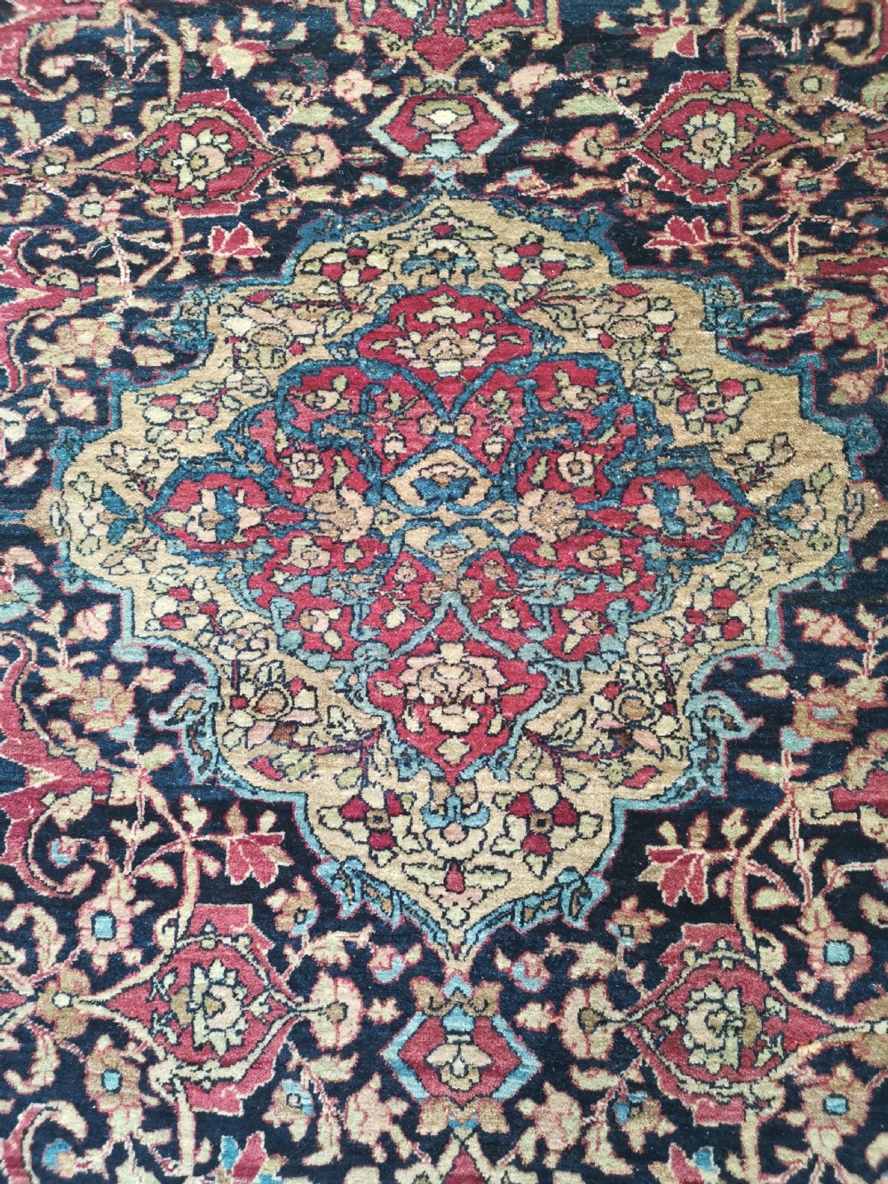 A rectangular hand-knotted Persian Isfahan rug featuring a central medallion with intricate floral arabesques in navy, deep red, and beige tones. View III