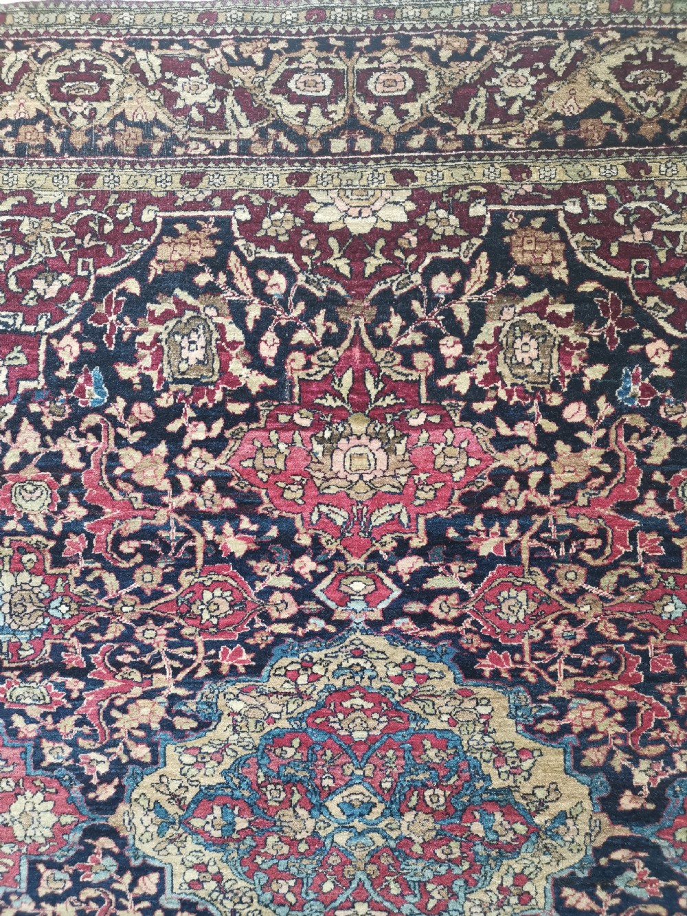 A rectangular hand-knotted Persian Isfahan rug featuring a central medallion with intricate floral arabesques in navy, deep red, and beige tones. View IV