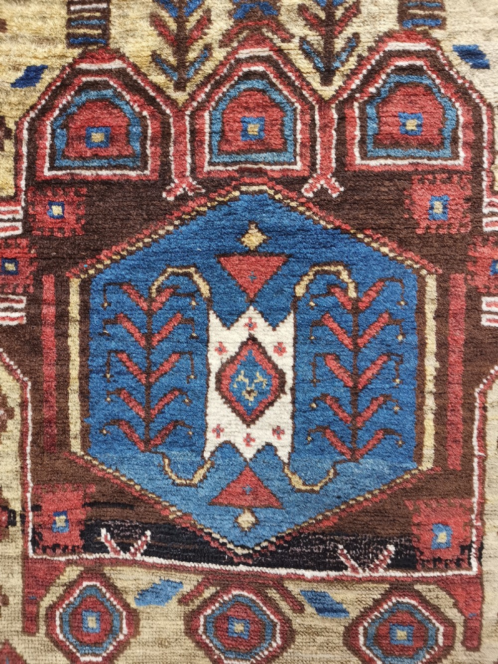 A hand-knotted North West Persian wool rug featuring a red field with two stacked geometric hexagonal medallions in blue and gold, surrounded by a navy border with abstract motifs. View II