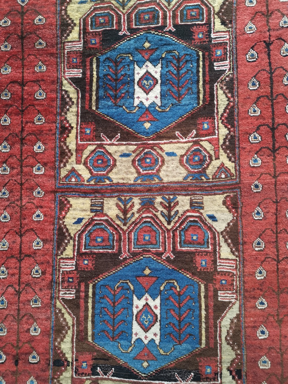 A hand-knotted North West Persian wool rug featuring a red field with two stacked geometric hexagonal medallions in blue and gold, surrounded by a navy border with abstract motifs. View III
