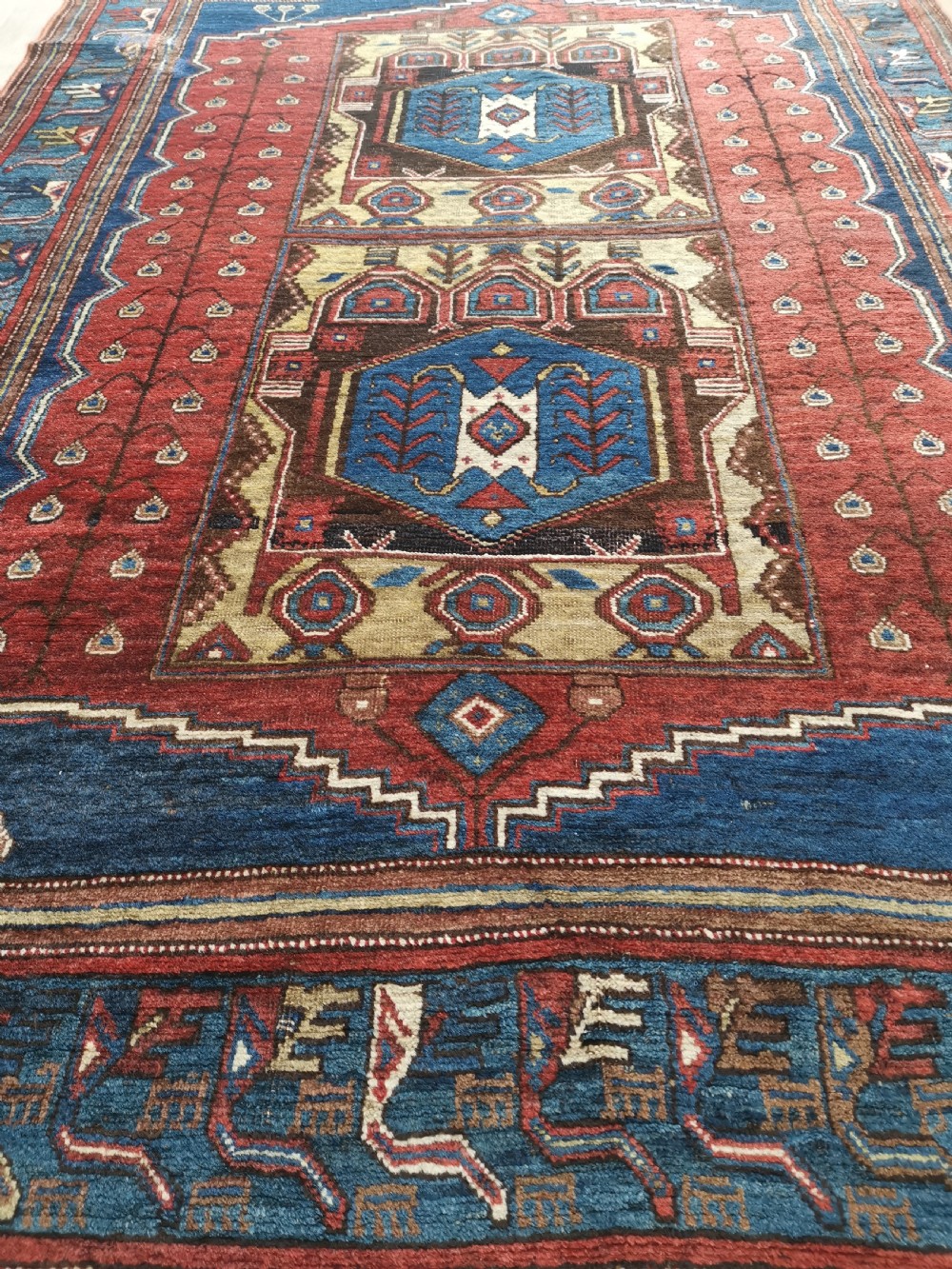 A hand-knotted North West Persian wool rug featuring a red field with two stacked geometric hexagonal medallions in blue and gold, surrounded by a navy border with abstract motifs. View V