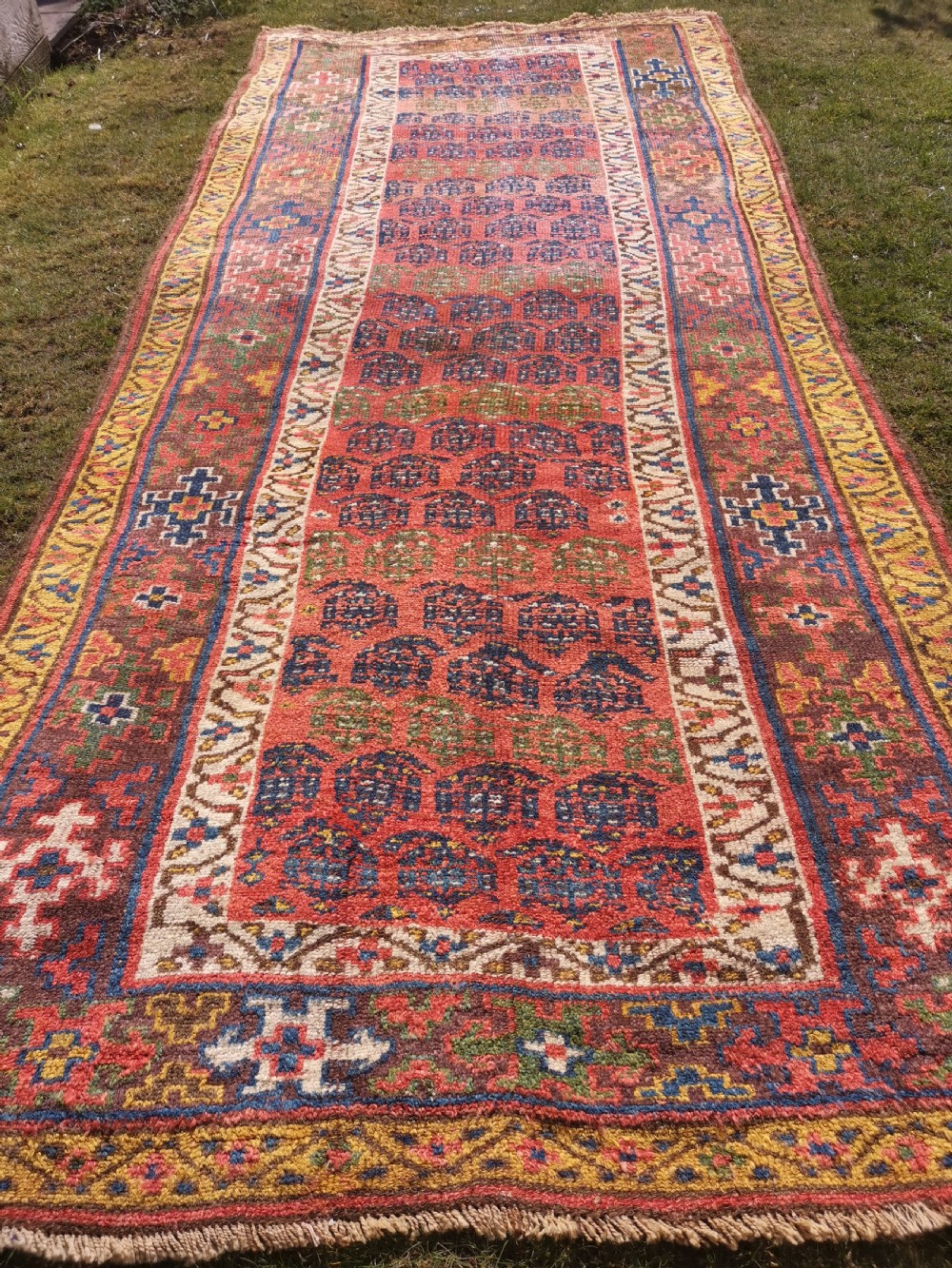 An antique hand-knotted Kurdish runner rug featuring repeating geometric field motifs in red, blue, and yellow with patterned tribal borders. View II