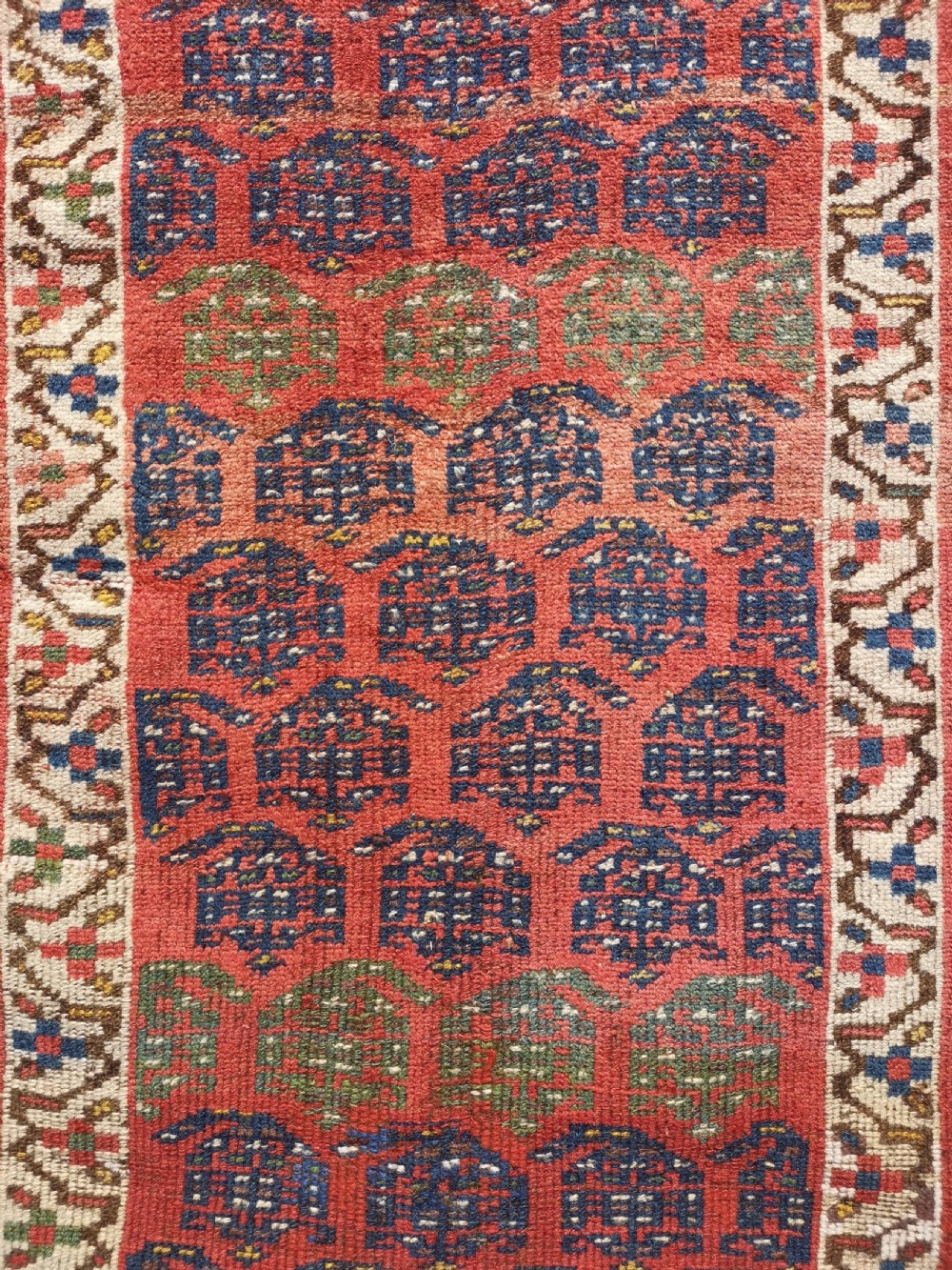 An antique hand-knotted Kurdish runner rug featuring repeating geometric field motifs in red, blue, and yellow with patterned tribal borders. View III