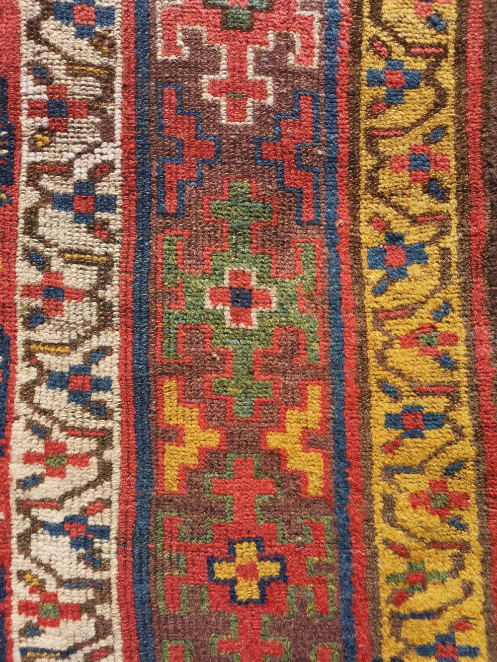 An antique hand-knotted Kurdish runner rug featuring repeating geometric field motifs in red, blue, and yellow with patterned tribal borders. View IV