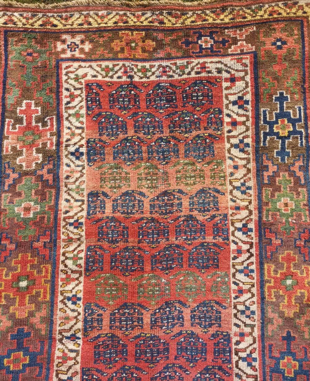 An antique hand-knotted Kurdish runner rug featuring repeating geometric field motifs in red, blue, and yellow with patterned tribal borders. View V