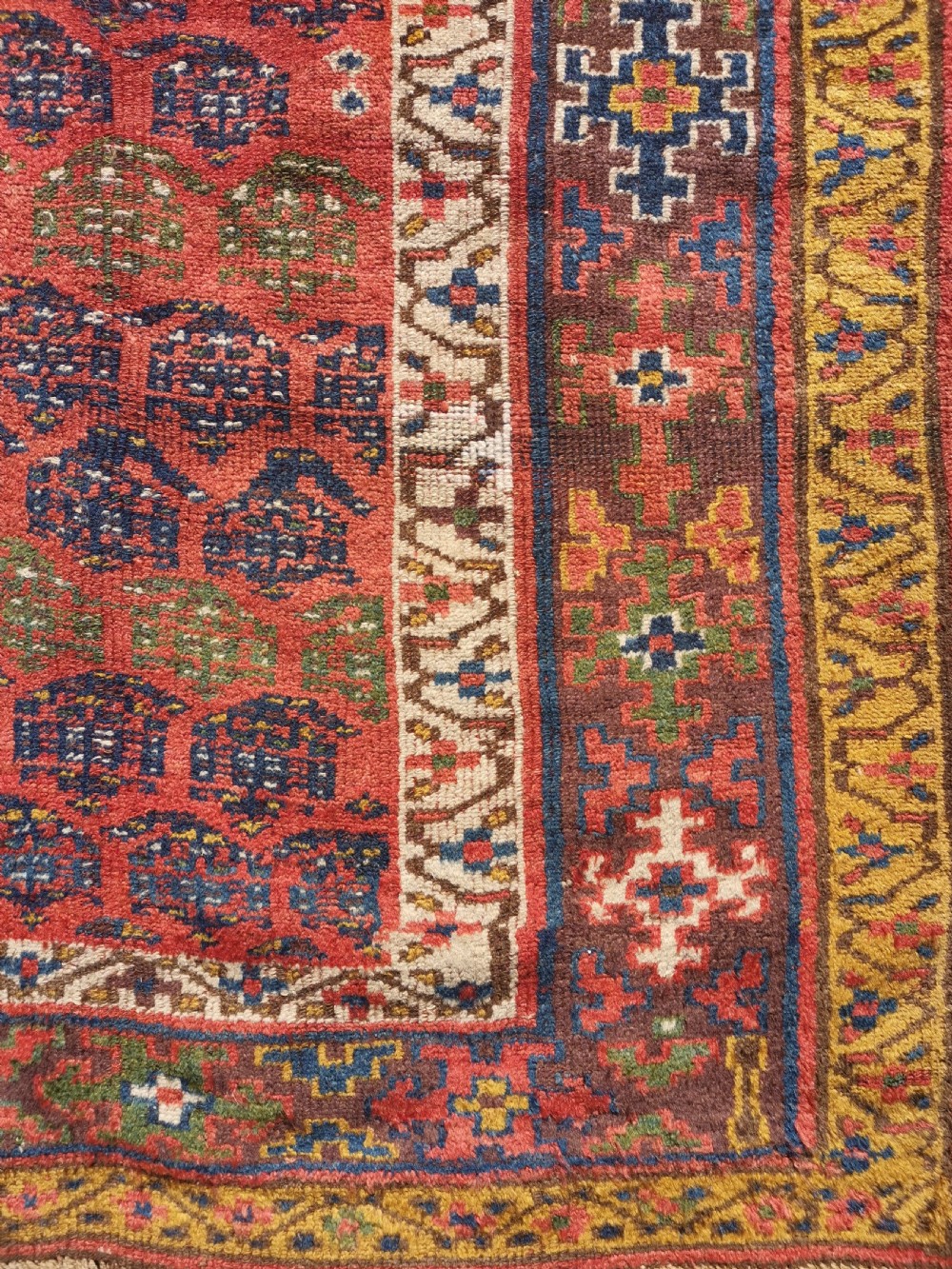 An antique hand-knotted Kurdish runner rug featuring repeating geometric field motifs in red, blue, and yellow with patterned tribal borders. View VI