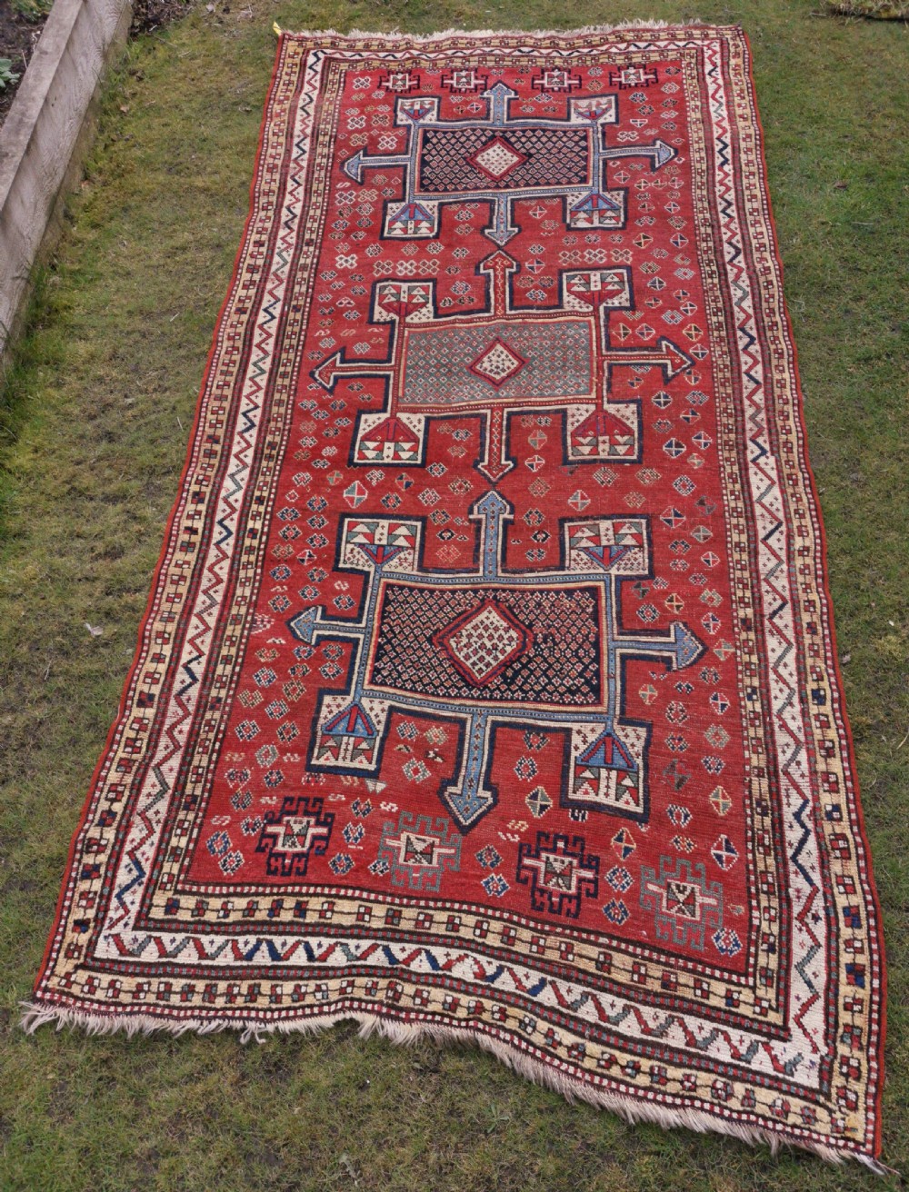 A hand-knotted tribal wool area rug featuring three central geometric stepped medallions in dark blue and ivory on a bold red field surrounded by patterned borders.