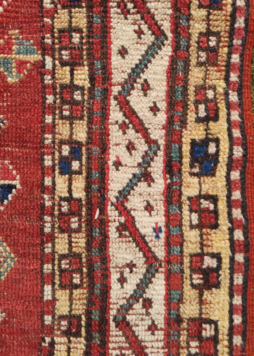 A hand-knotted tribal wool area rug featuring three central geometric stepped medallions in dark blue and ivory on a bold red field surrounded by patterned borders. View V
