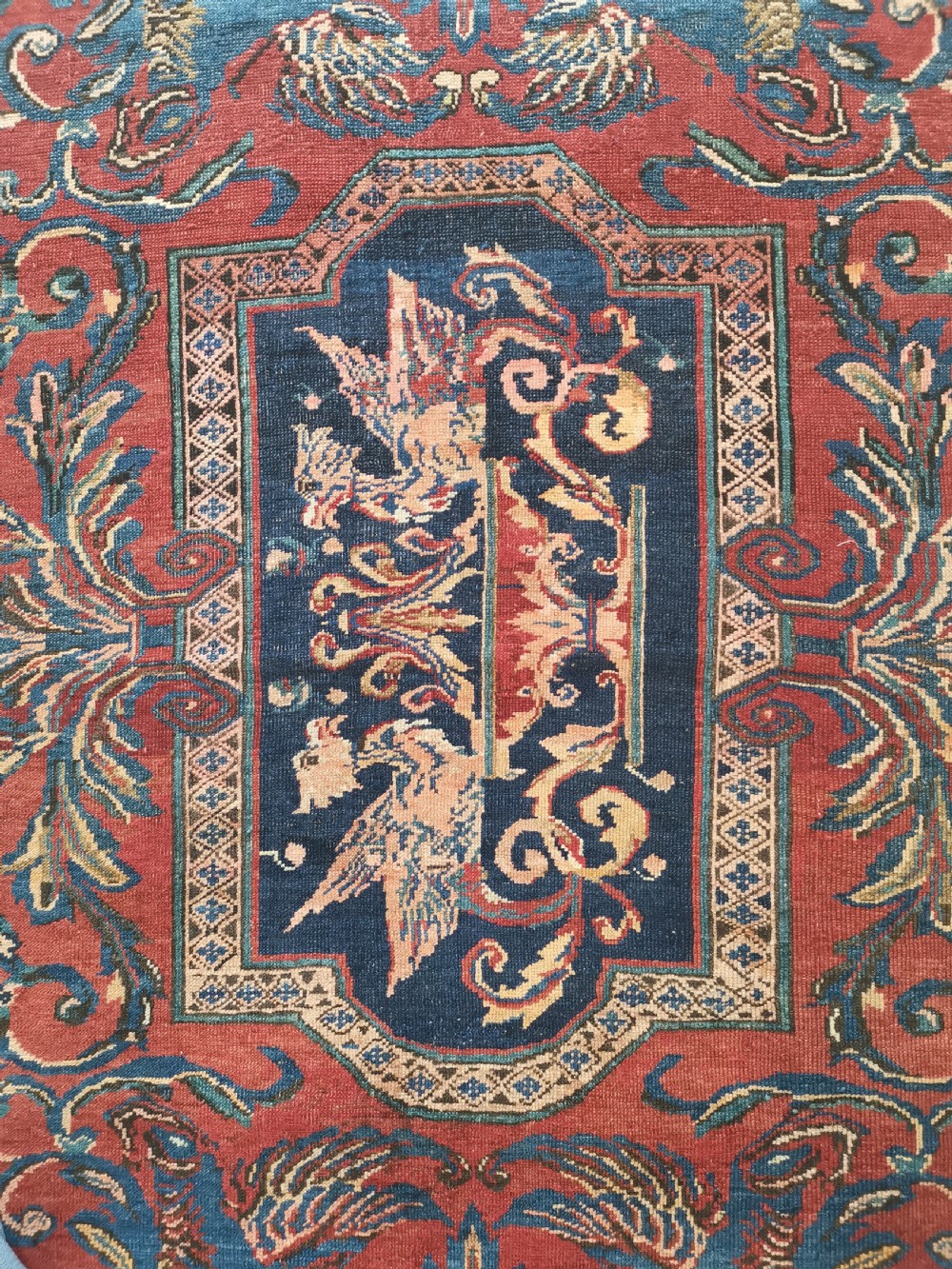 An antique hand-knotted Karabagh wool rug featuring a red field, a dark blue central medallion, floral scrolling branches, and stylised bird motifs surrounded by a geometric border. View II