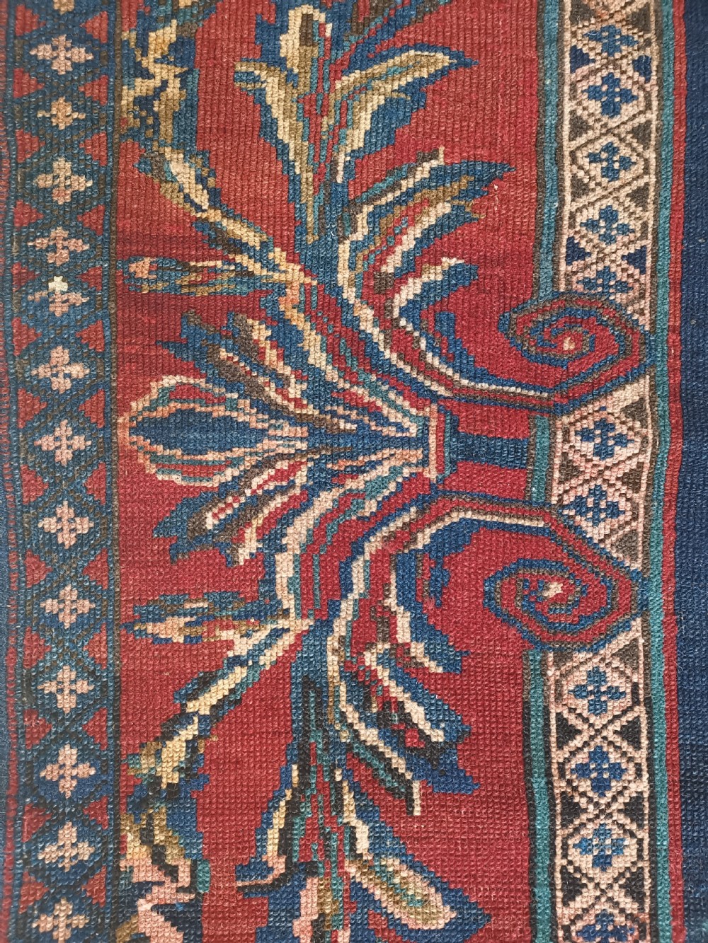 An antique hand-knotted Karabagh wool rug featuring a red field, a dark blue central medallion, floral scrolling branches, and stylised bird motifs surrounded by a geometric border. View III