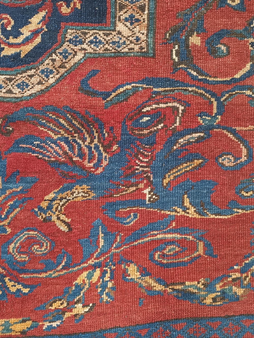 An antique hand-knotted Karabagh wool rug featuring a red field, a dark blue central medallion, floral scrolling branches, and stylised bird motifs surrounded by a geometric border. View IV