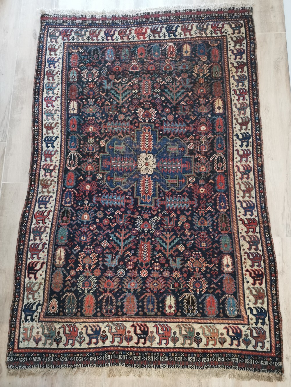 A rectangular hand-knotted wool rug featuring a dark navy central field with a large blue geometric medallion, surrounded by stylised bird motifs and a cream pattern border.
