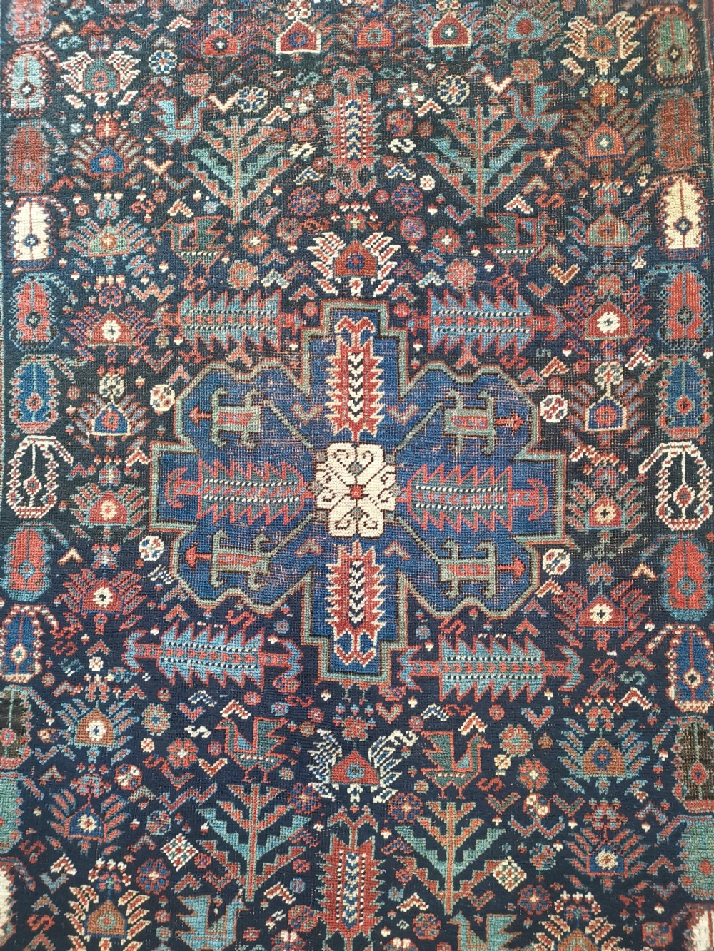 A rectangular hand-knotted wool rug featuring a dark navy central field with a large blue geometric medallion, surrounded by stylised bird motifs and a cream pattern border. View II