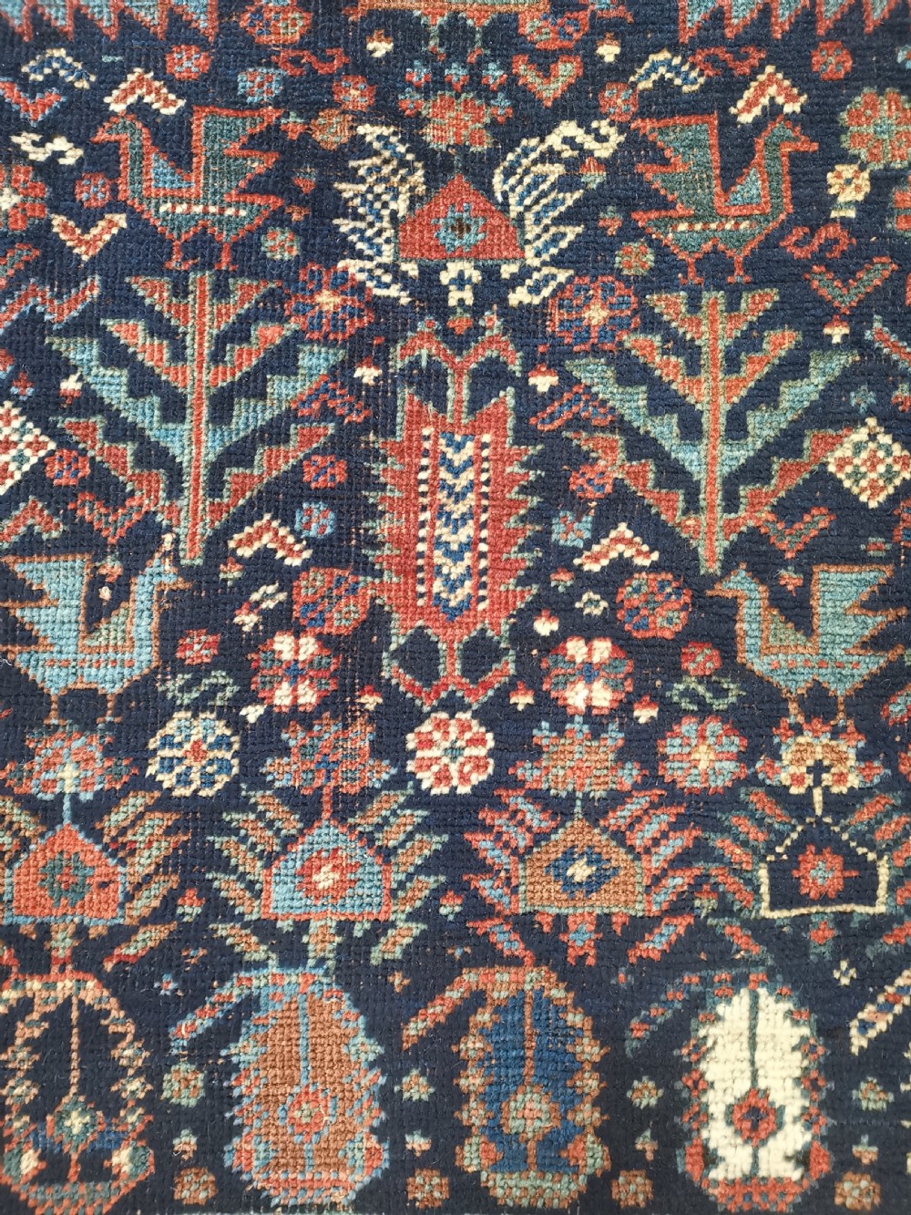 A rectangular hand-knotted wool rug featuring a dark navy central field with a large blue geometric medallion, surrounded by stylised bird motifs and a cream pattern border. View III