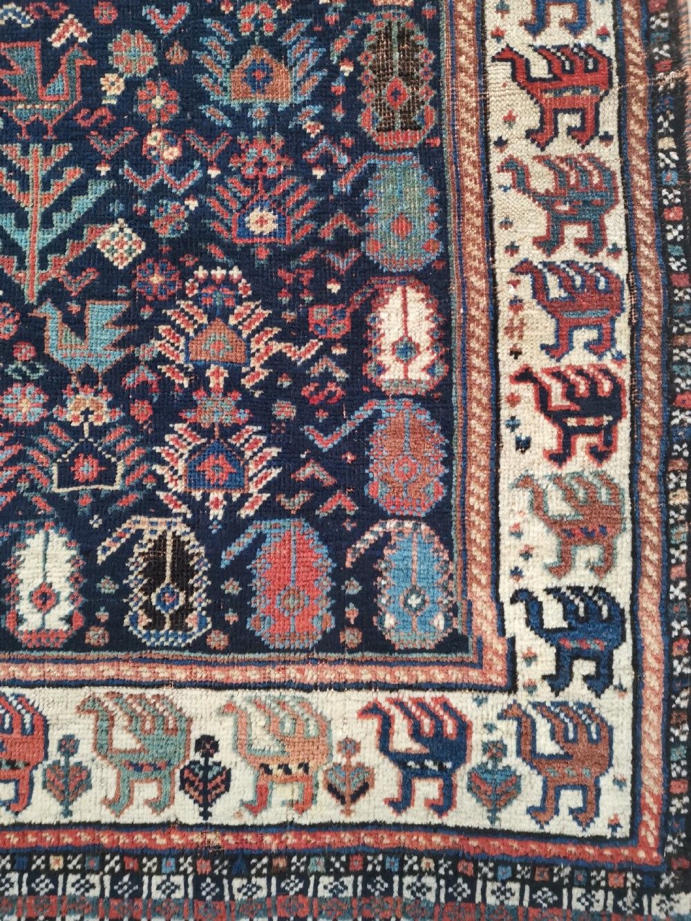 A rectangular hand-knotted wool rug featuring a dark navy central field with a large blue geometric medallion, surrounded by stylised bird motifs and a cream pattern border. View IV
