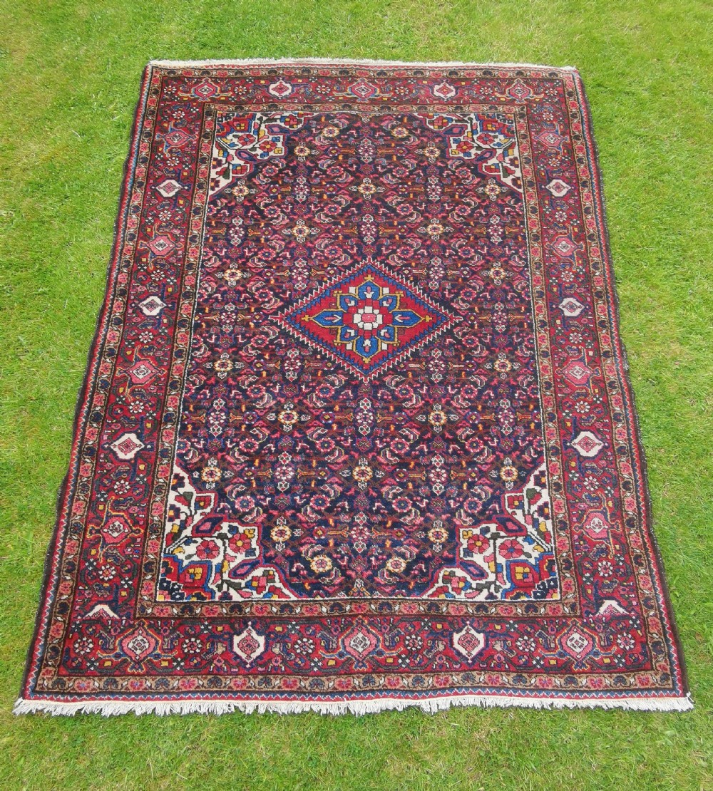 A hand-knotted Persian Hamadan wool rug featuring a central red and blue diamond medallion set on an indigo floral field with a red geometric border.