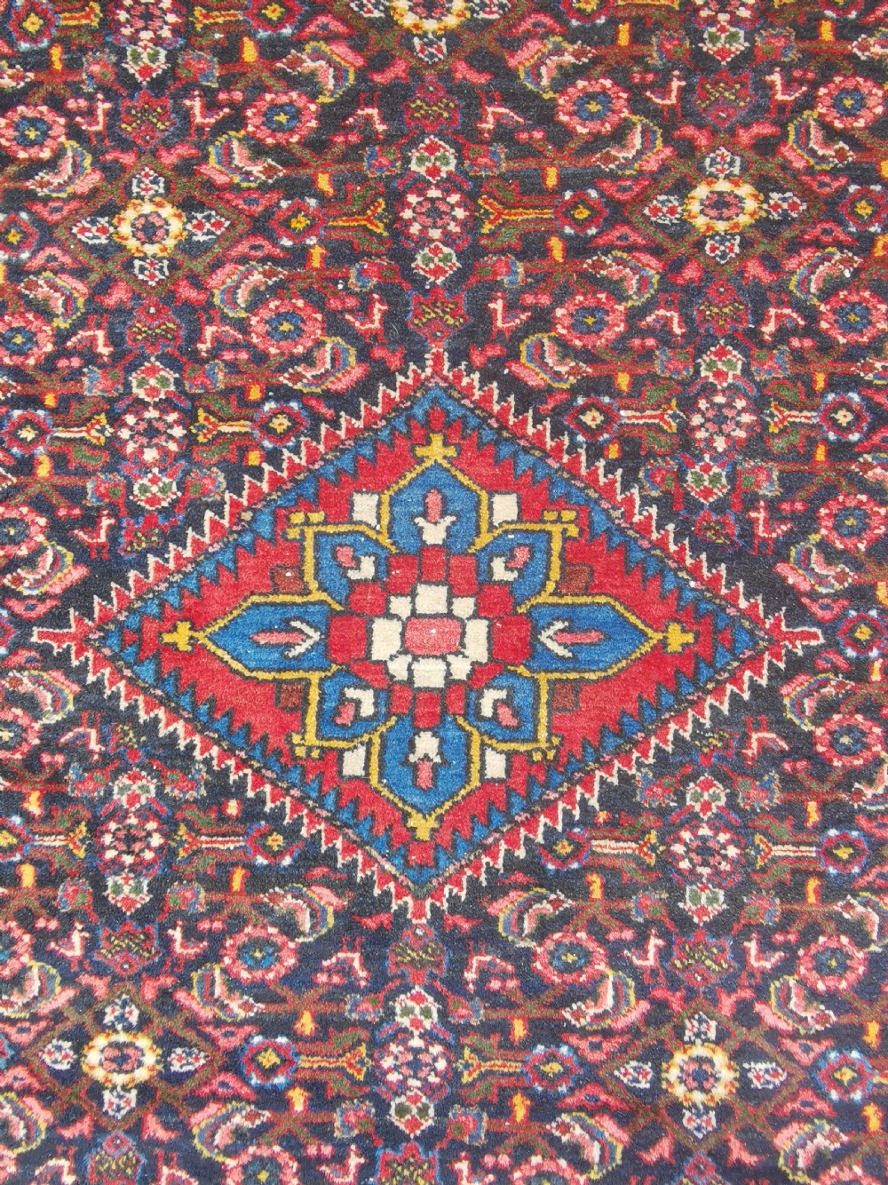 A hand-knotted Persian Hamadan wool rug featuring a central red and blue diamond medallion set on an indigo floral field with a red geometric border. View III