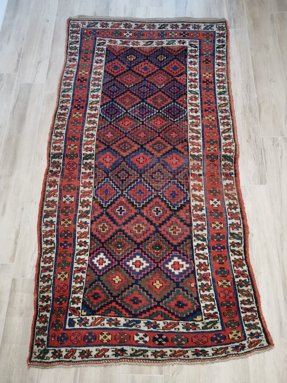 An antique Shahsavan handwoven wool runner featuring a red and navy blue geometric diamond lattice pattern surrounded by multi-coloured borders.