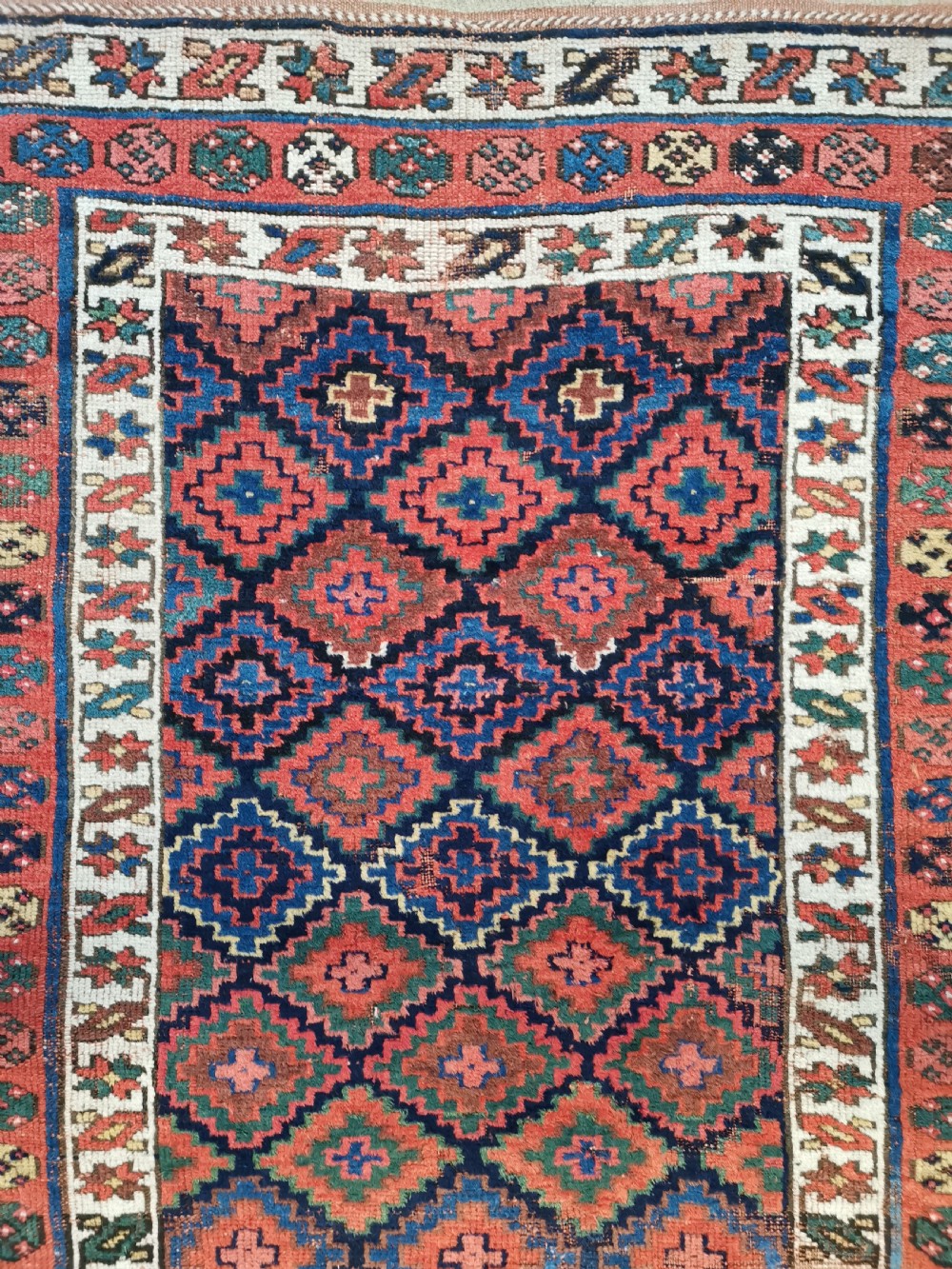 An antique Shahsavan handwoven wool runner featuring a red and navy blue geometric diamond lattice pattern surrounded by multi-coloured borders. View V