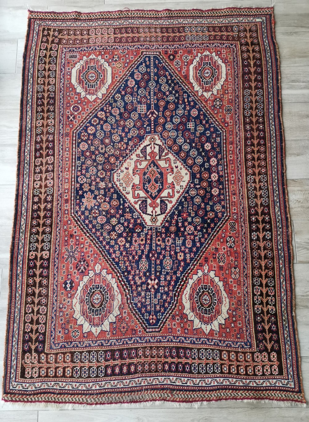 A hand-knotted antique Qashqai wool rug featuring a central indigo diamond medallion surrounded by a terracotta field and geometric borders.