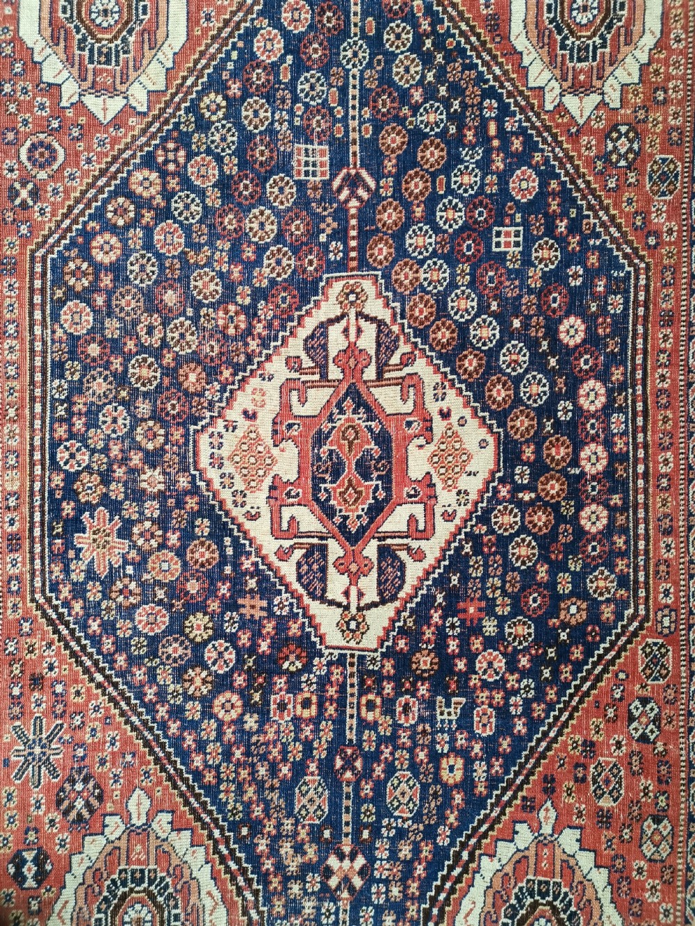 A hand-knotted antique Qashqai wool rug featuring a central indigo diamond medallion surrounded by a terracotta field and geometric borders. View II