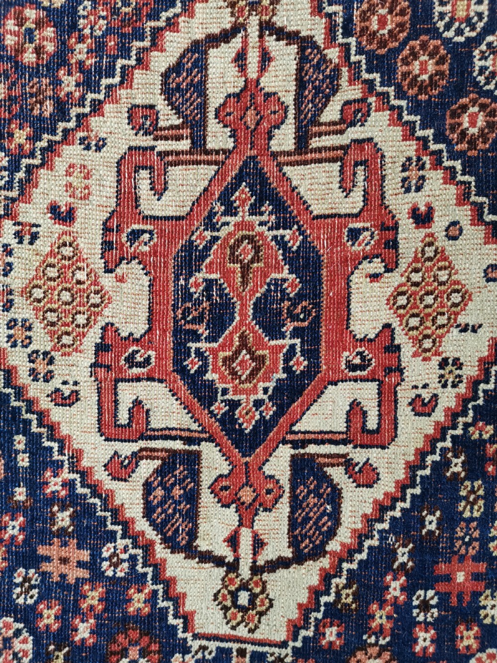 A hand-knotted antique Qashqai wool rug featuring a central indigo diamond medallion surrounded by a terracotta field and geometric borders. View III