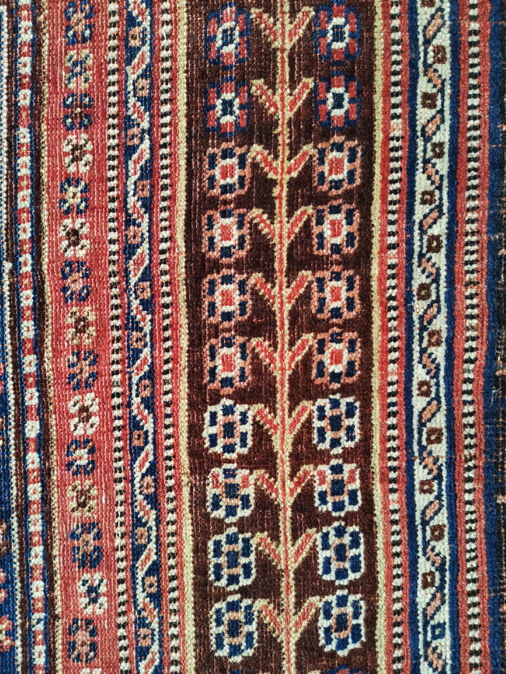 A hand-knotted antique Qashqai wool rug featuring a central indigo diamond medallion surrounded by a terracotta field and geometric borders. View V