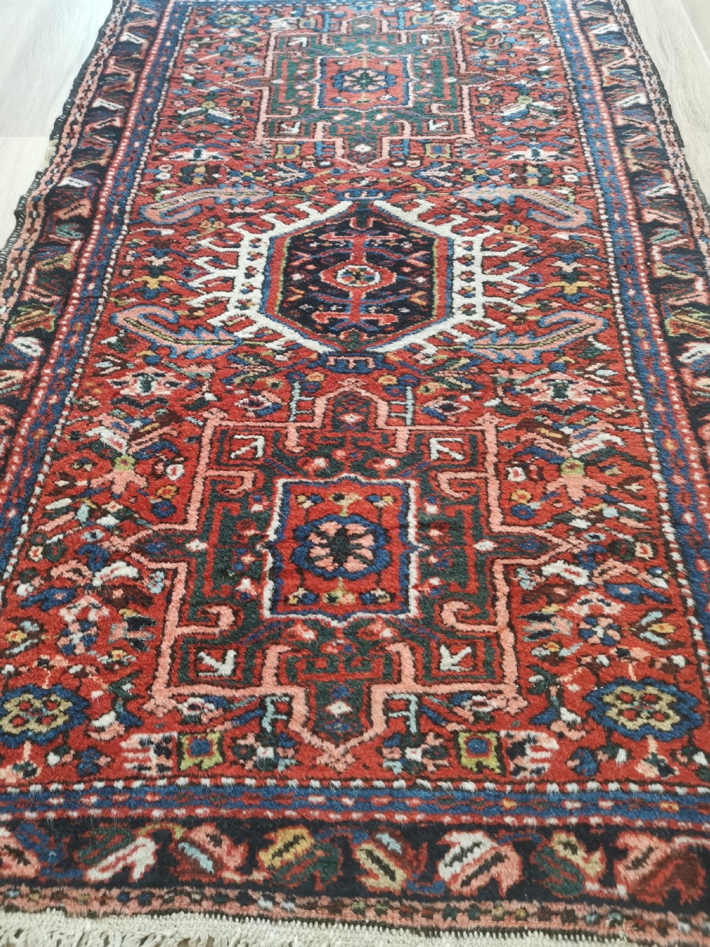 A hand-knotted wool Karaja rug featuring a primary red field with three central geometric medallions, surrounded by multi-layered borders in navy, green, and ivory tones. View III