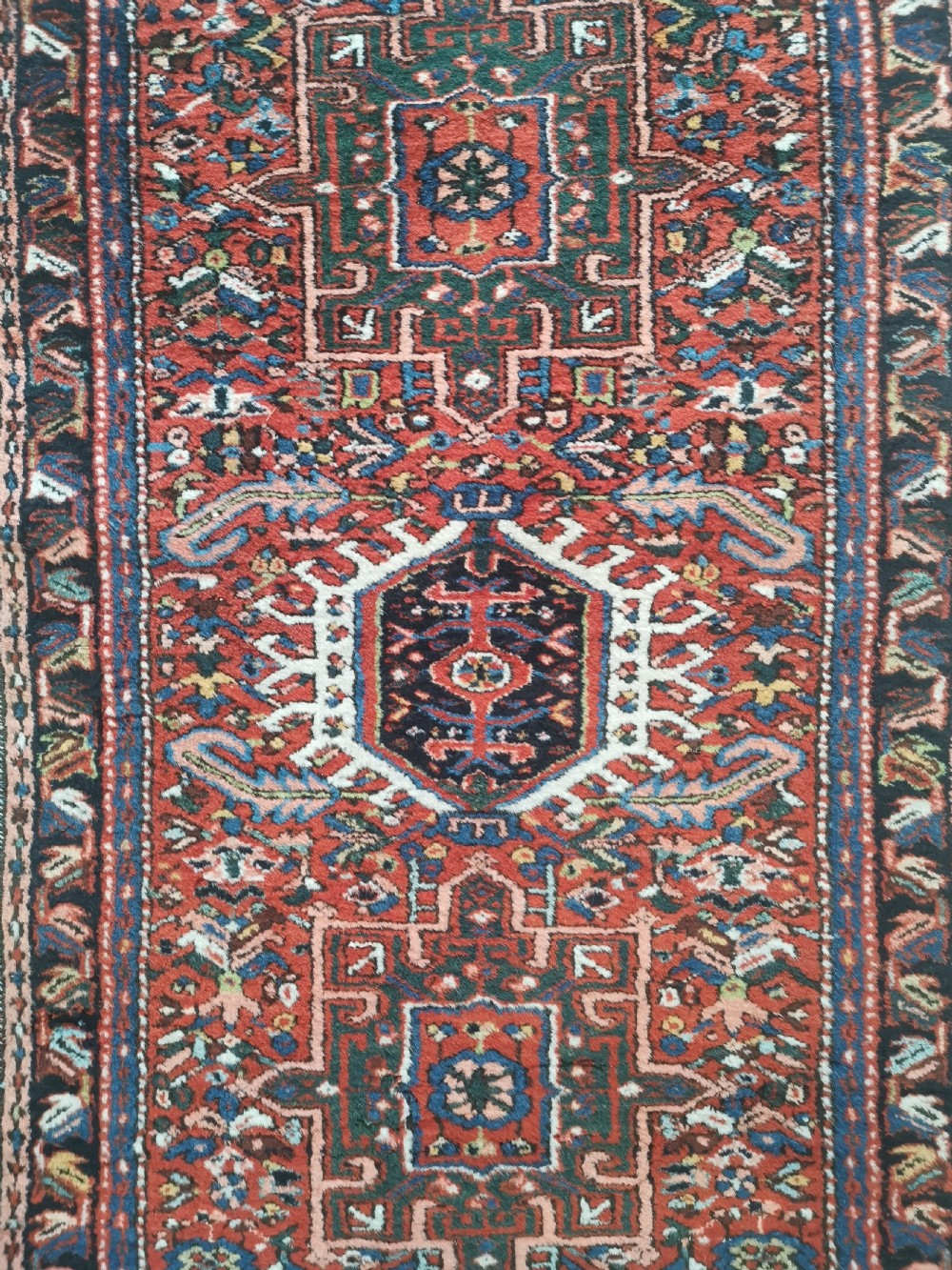 A hand-knotted wool Karaja rug featuring a primary red field with three central geometric medallions, surrounded by multi-layered borders in navy, green, and ivory tones. View IV