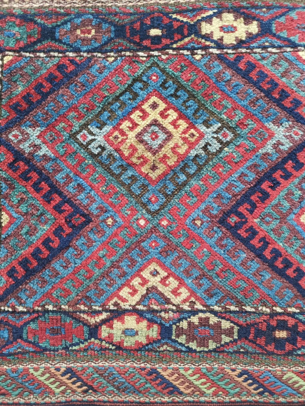 A square handwoven antique Kurdish bagface featuring a central diamond motif surrounded by geometric patterns in red, blue, green, and cream wool. View II