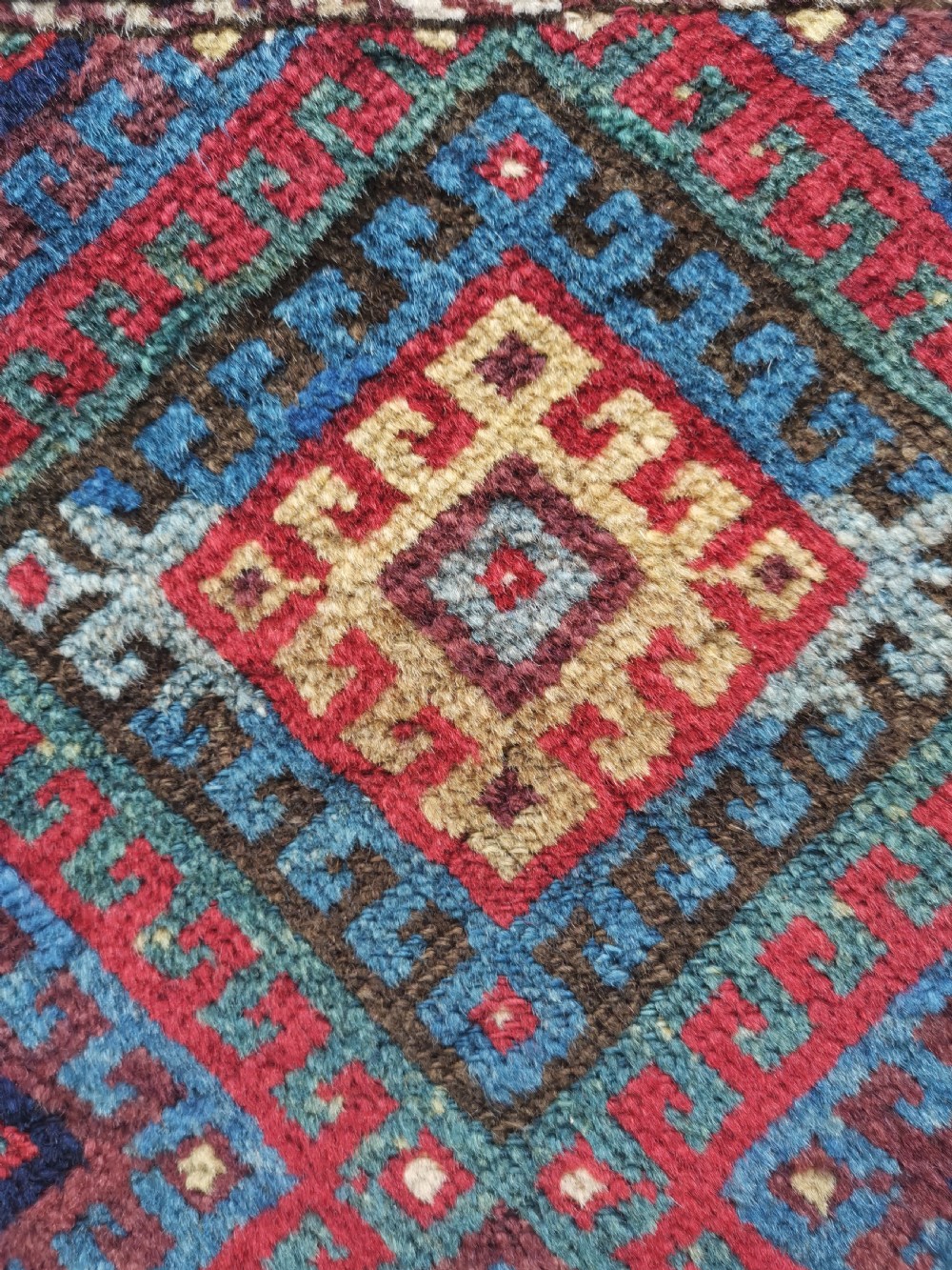 A square handwoven antique Kurdish bagface featuring a central diamond motif surrounded by geometric patterns in red, blue, green, and cream wool. View III