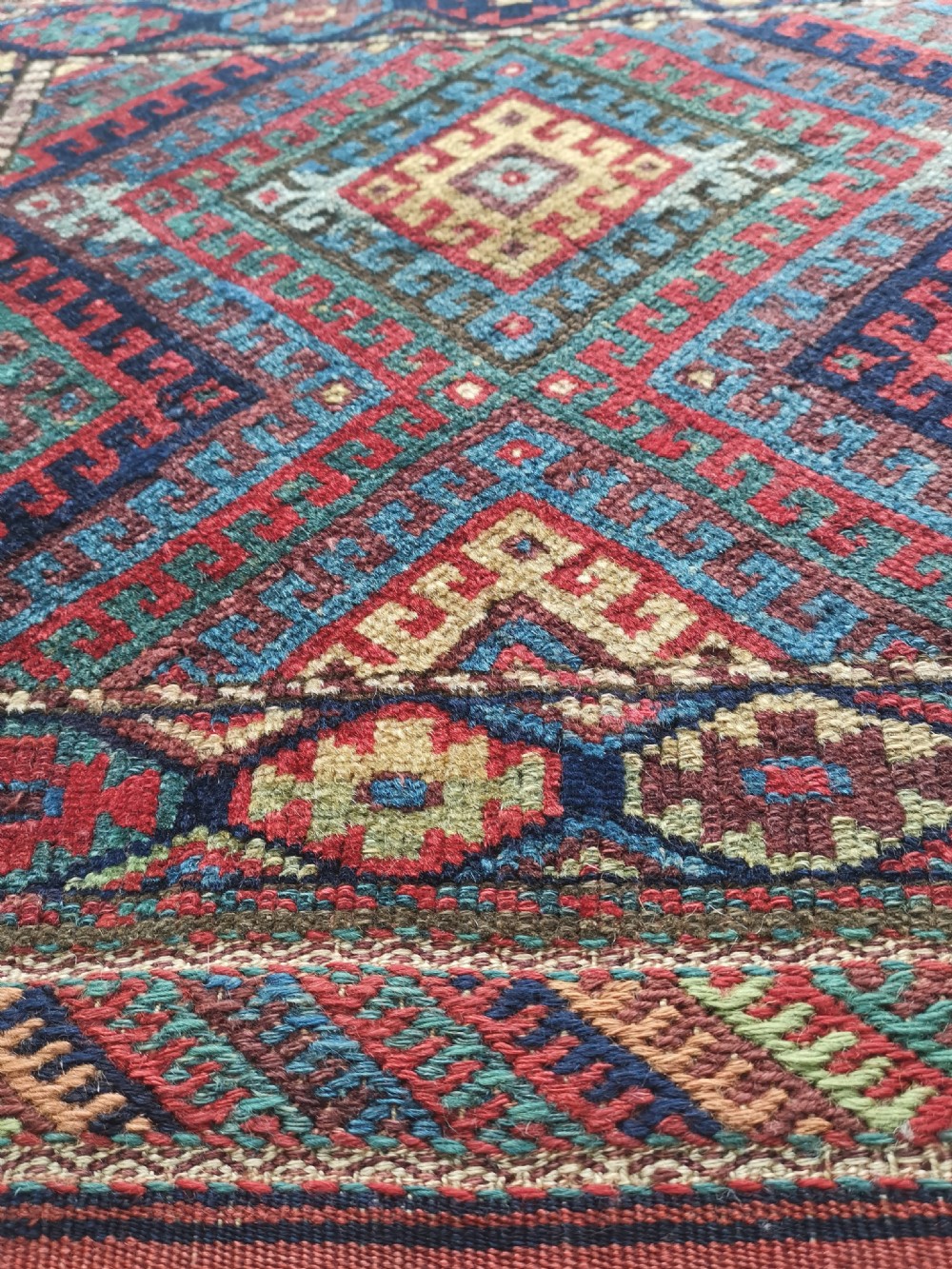 A square handwoven antique Kurdish bagface featuring a central diamond motif surrounded by geometric patterns in red, blue, green, and cream wool. View IV