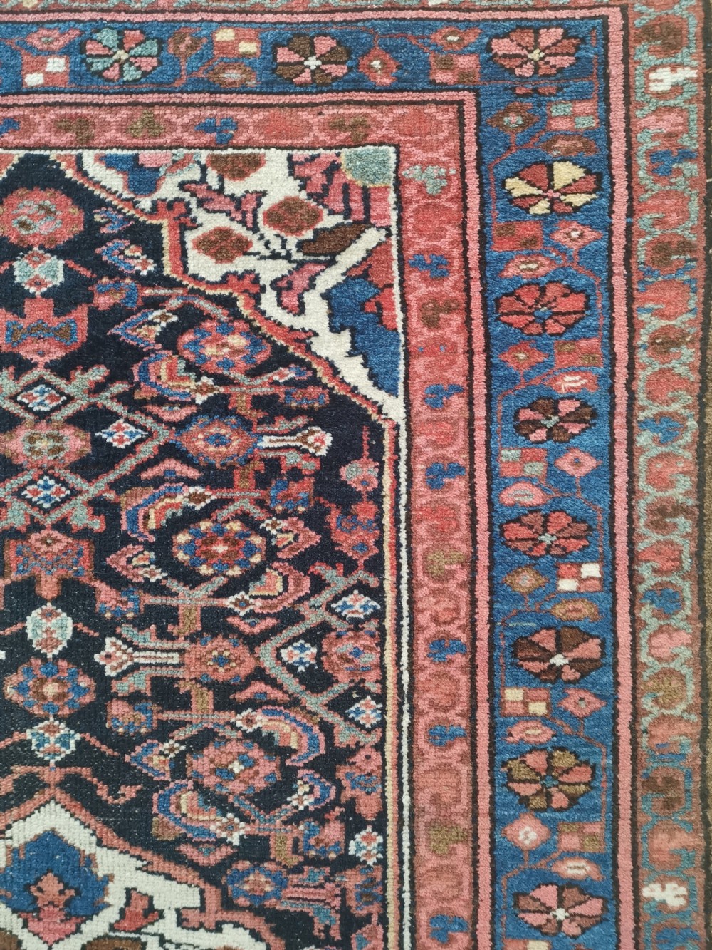 A rectangular hand-knotted wool rug featuring a central cream diamond medallion surrounded by a dark navy field with intricate geometric floral motifs and reddish-pink and blue borders. View II