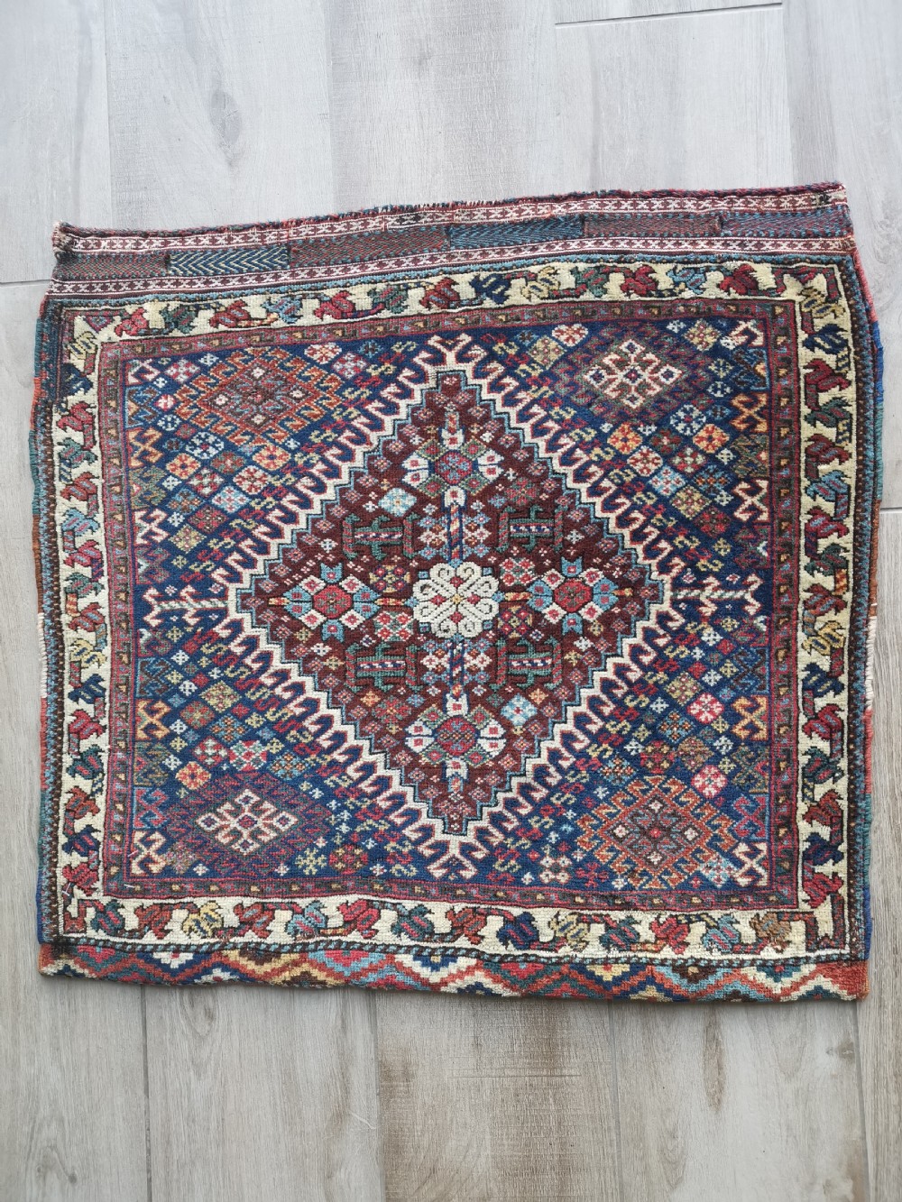 A square hand-knotted wool Qashqai bagface featuring a central geometric diamond medallion surrounded by patterned borders in red, navy blue, and cream shades.