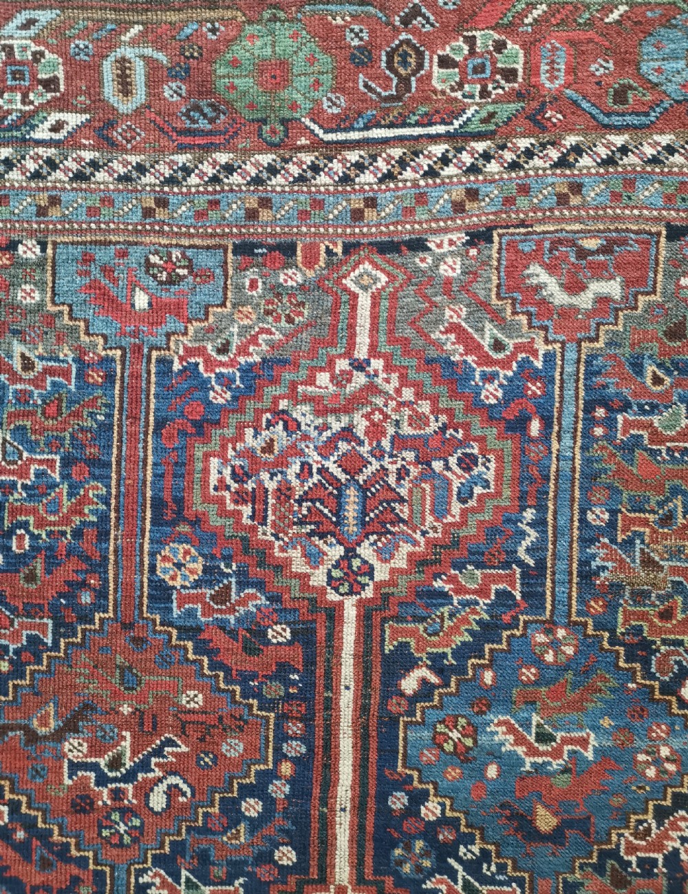 An antique Khamseh hand-knotted wool rug featuring geometric diamond medallions, stylized bird motifs, and a rich navy blue and madder red palette. View III