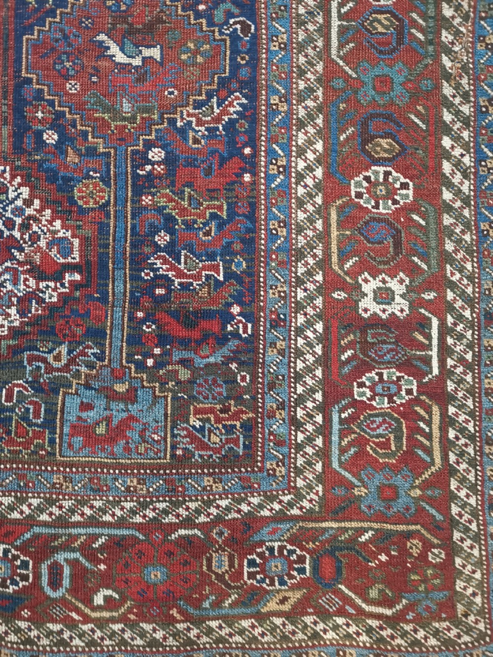 An antique Khamseh hand-knotted wool rug featuring geometric diamond medallions, stylized bird motifs, and a rich navy blue and madder red palette. View IV
