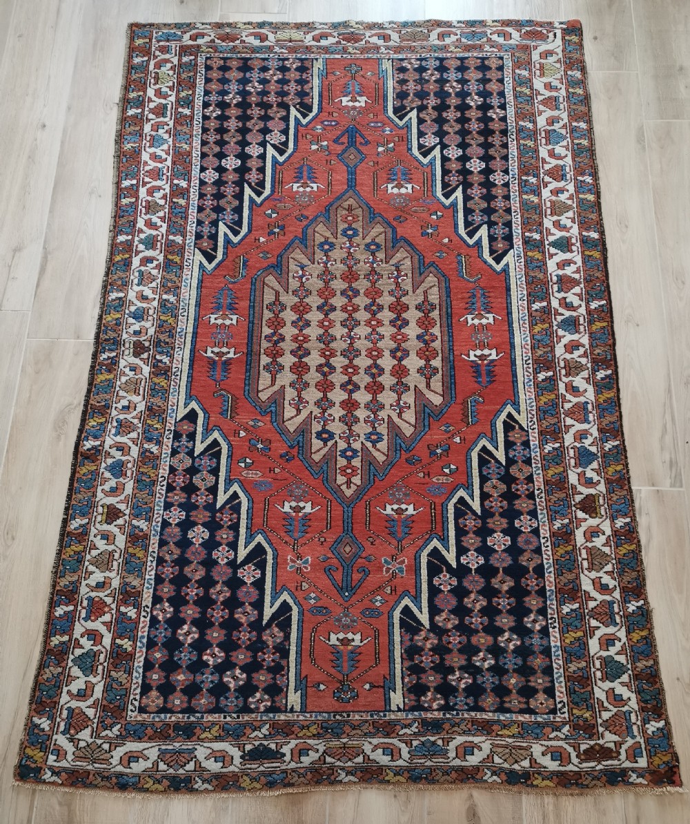 A hand-knotted Mazlaghan wool rug featuring a terracotta stepped central medallion surrounded by a dark blue geometric field and intricate multi-layered borders.