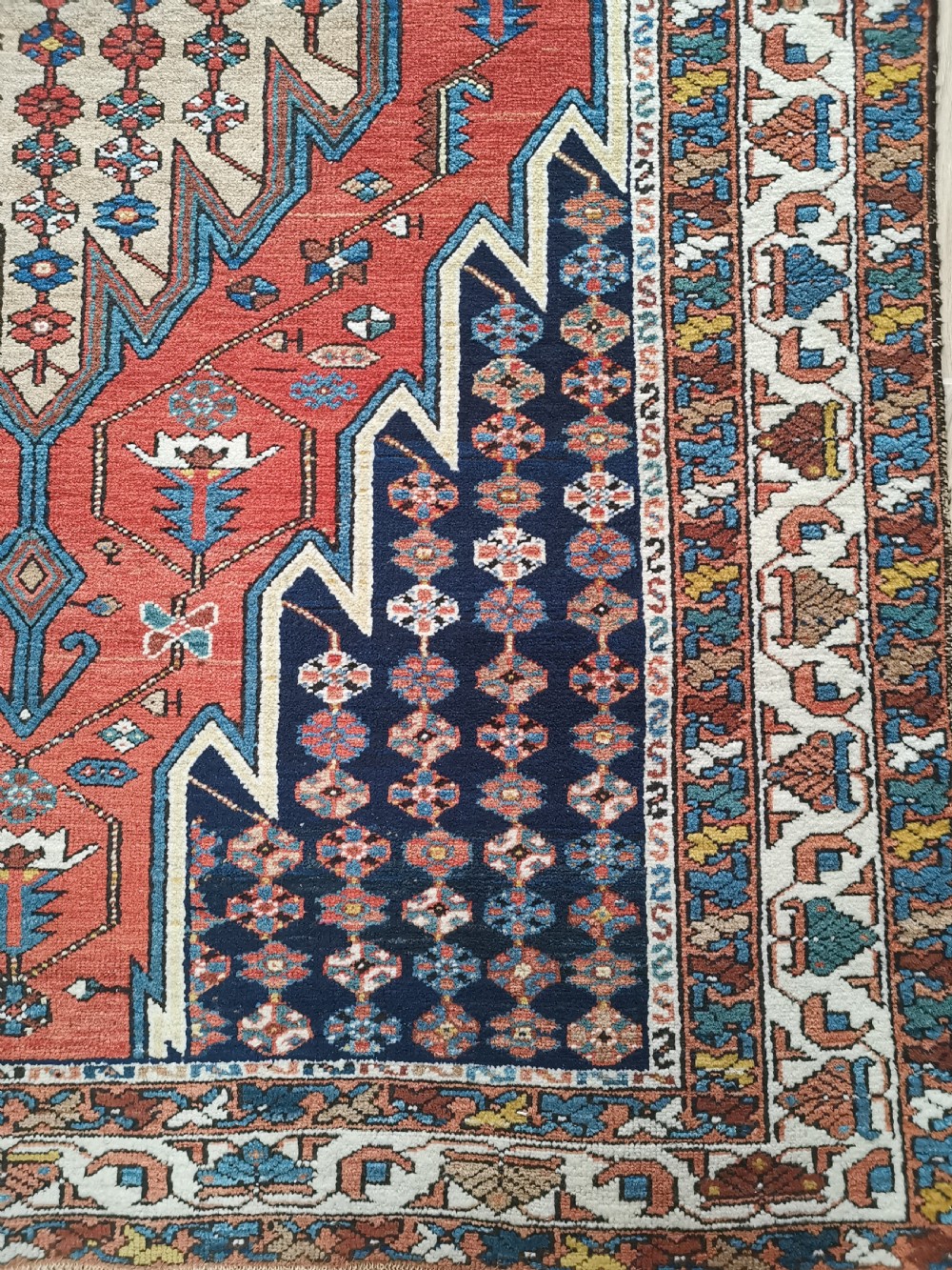 A hand-knotted Mazlaghan wool rug featuring a terracotta stepped central medallion surrounded by a dark blue geometric field and intricate multi-layered borders. View IV