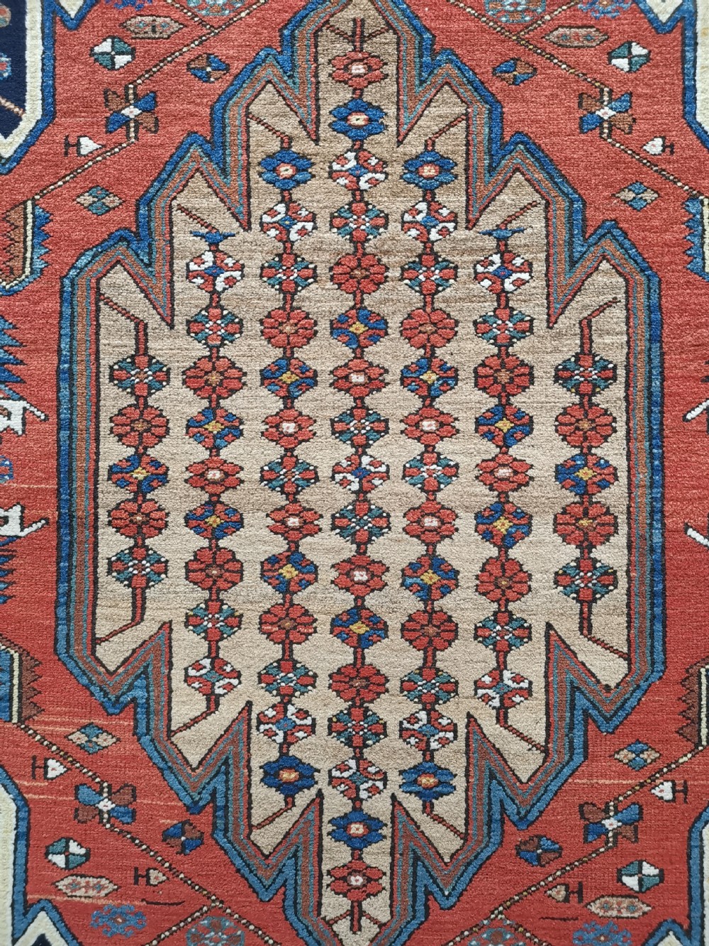 A hand-knotted Mazlaghan wool rug featuring a terracotta stepped central medallion surrounded by a dark blue geometric field and intricate multi-layered borders. View V