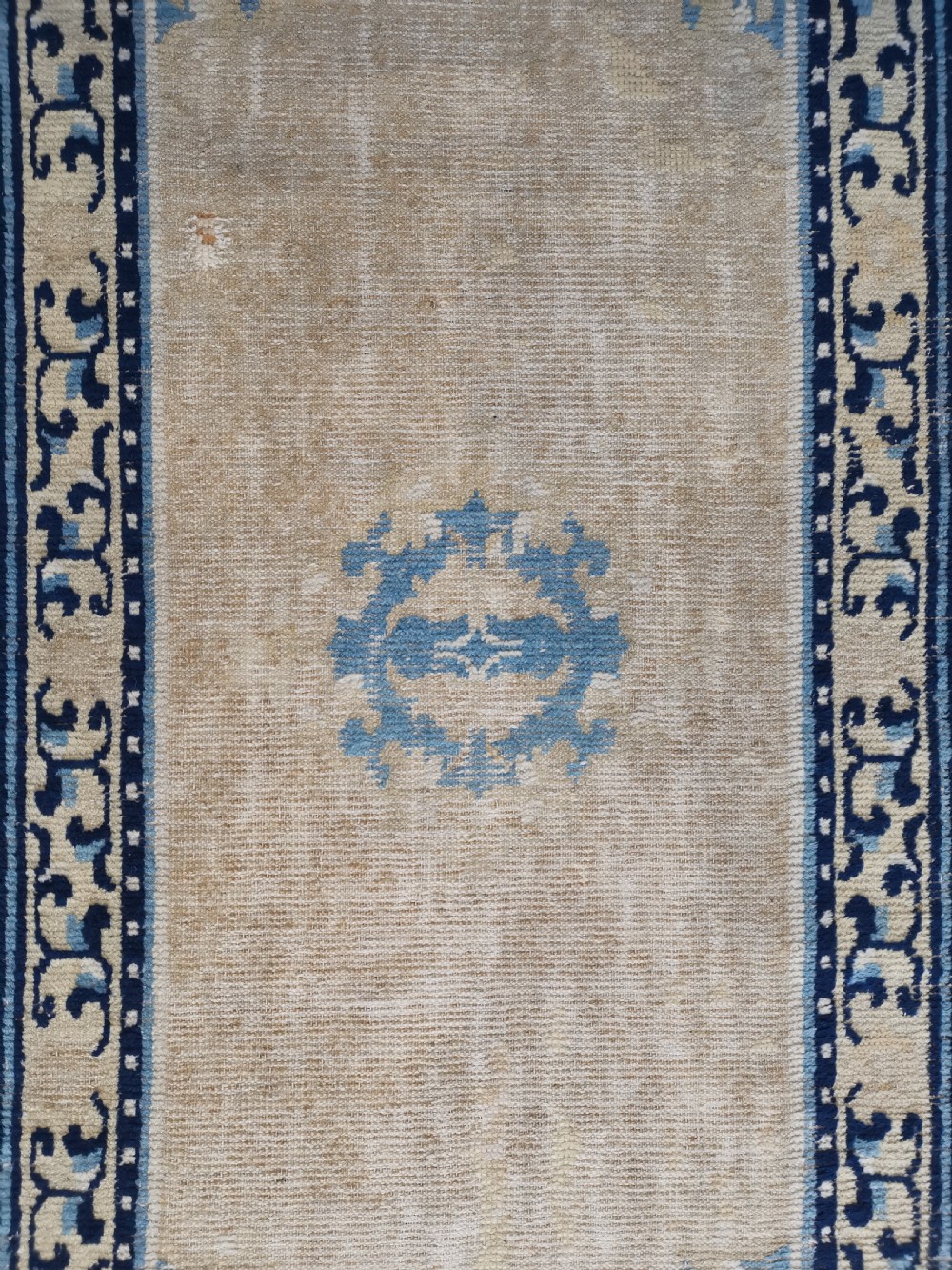 A hand-knotted antique Ningxia rug featuring a beige wool field, central blue medallion, corner motifs, and a repeating scrolling blue border. View II