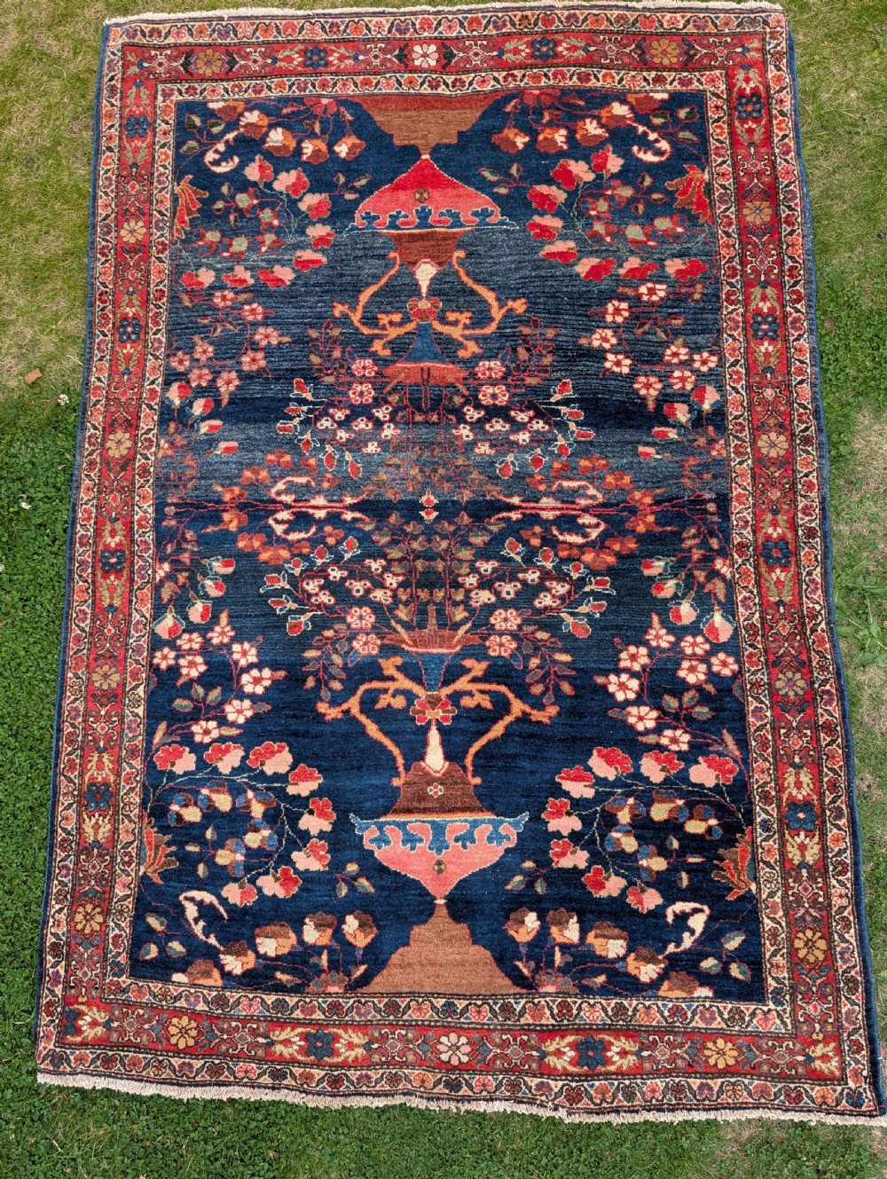 A hand-knotted Persian Kashan wool rug featuring a dark blue field filled with floral vase motifs and framed by a red floral border.