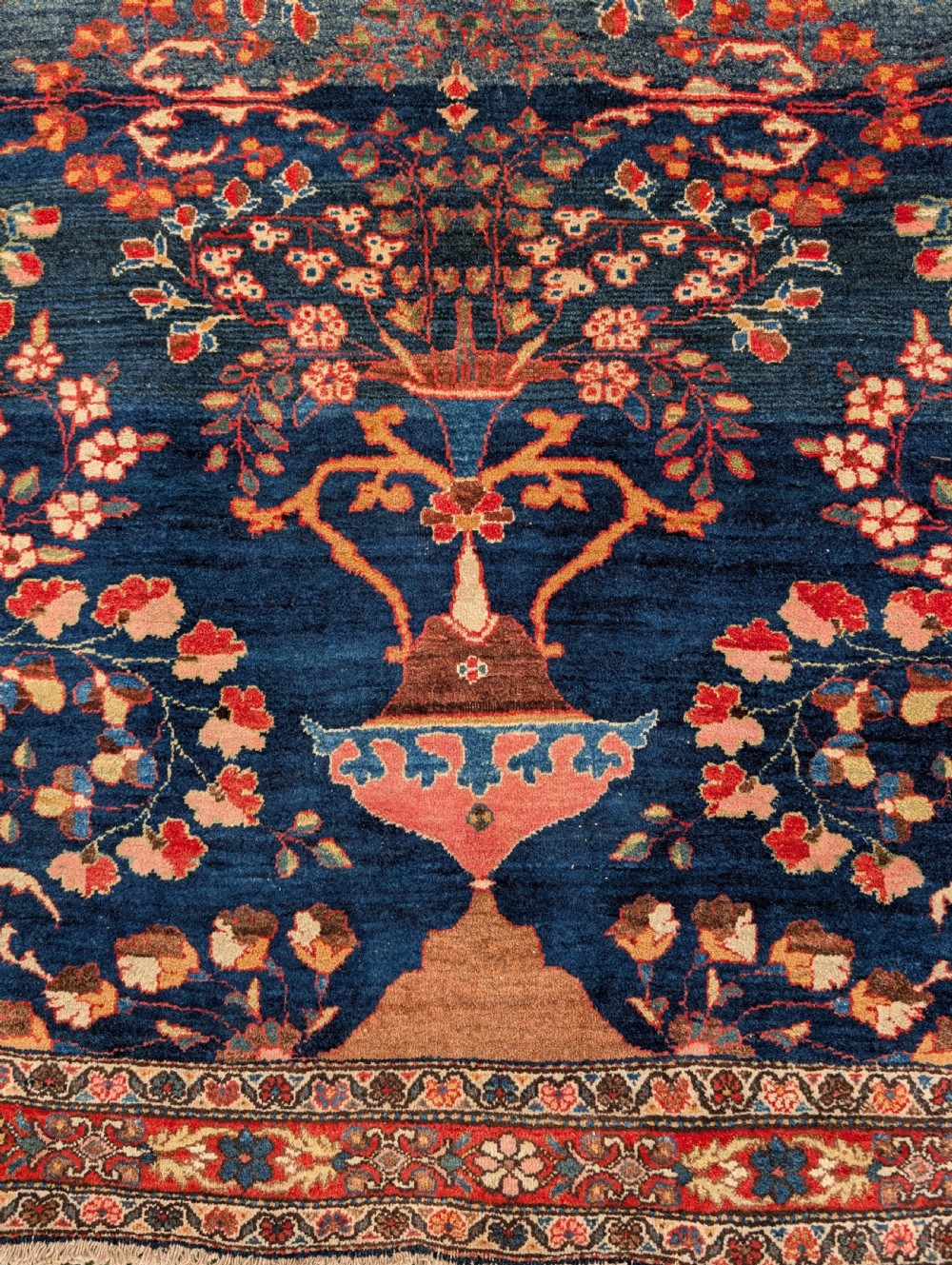A hand-knotted Persian Kashan wool rug featuring a dark blue field filled with floral vase motifs and framed by a red floral border. View III