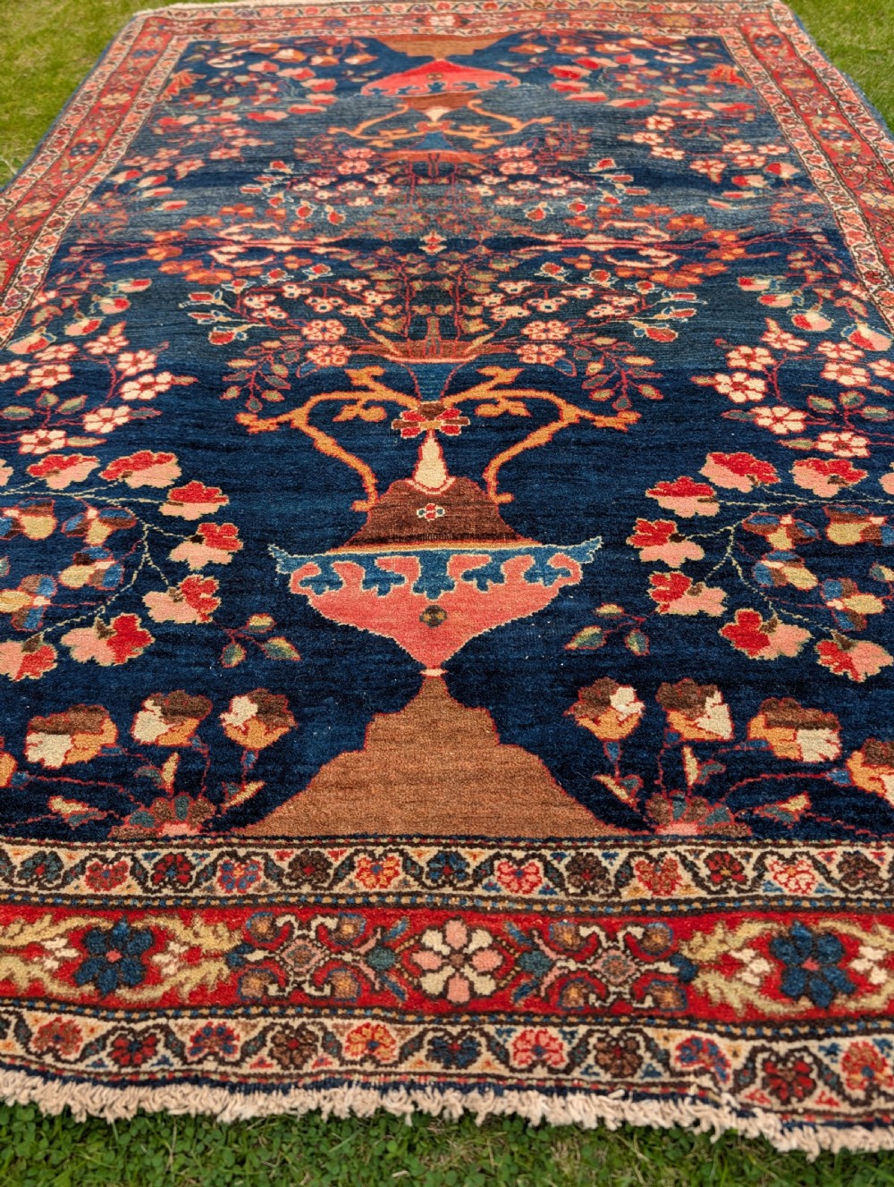 A hand-knotted Persian Kashan wool rug featuring a dark blue field filled with floral vase motifs and framed by a red floral border. View IV