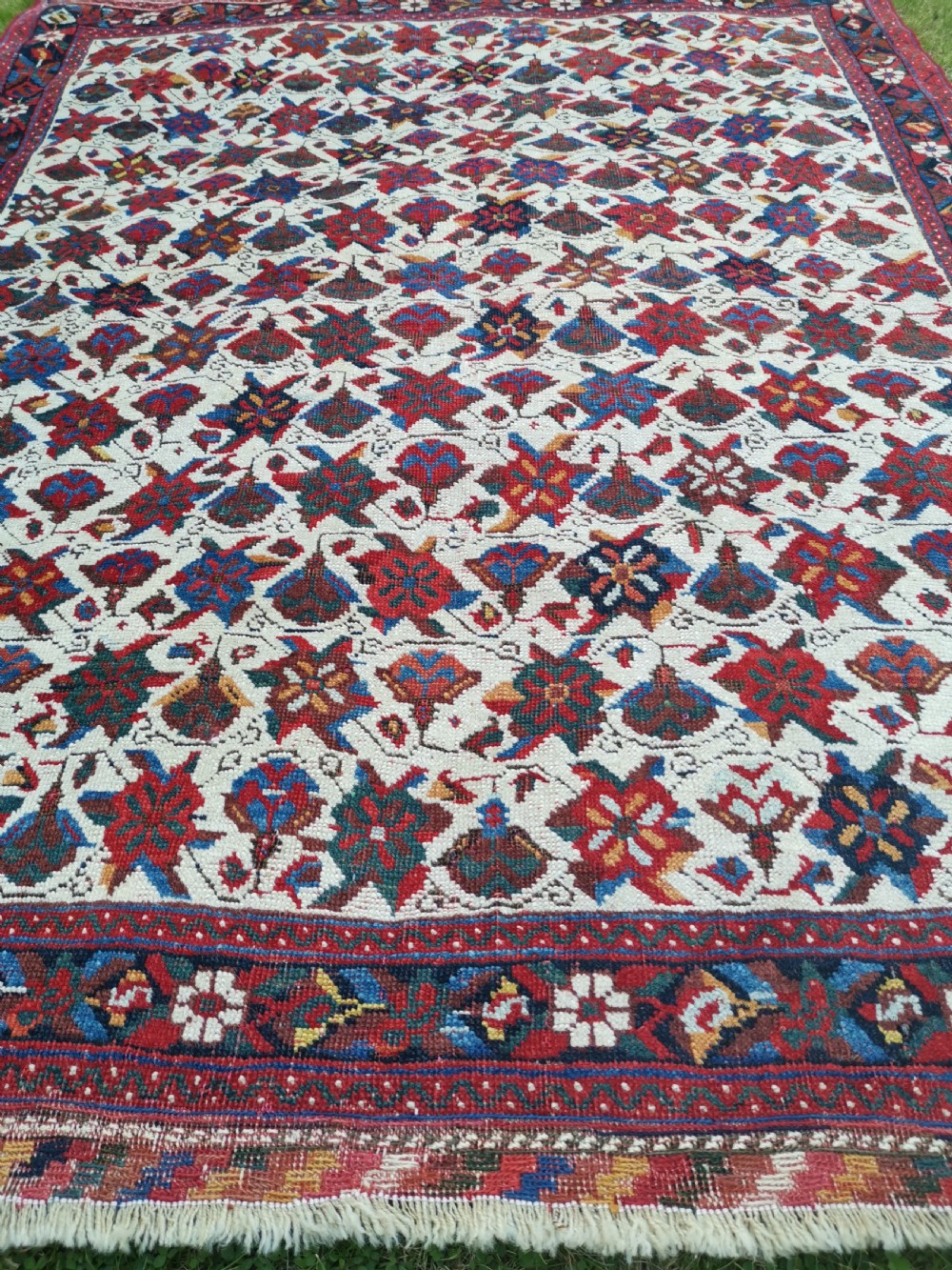 An antique hand-knotted Afshar wool rug featuring a cream field with repeating red and navy geometric motifs framed by a dark red patterned border. View V