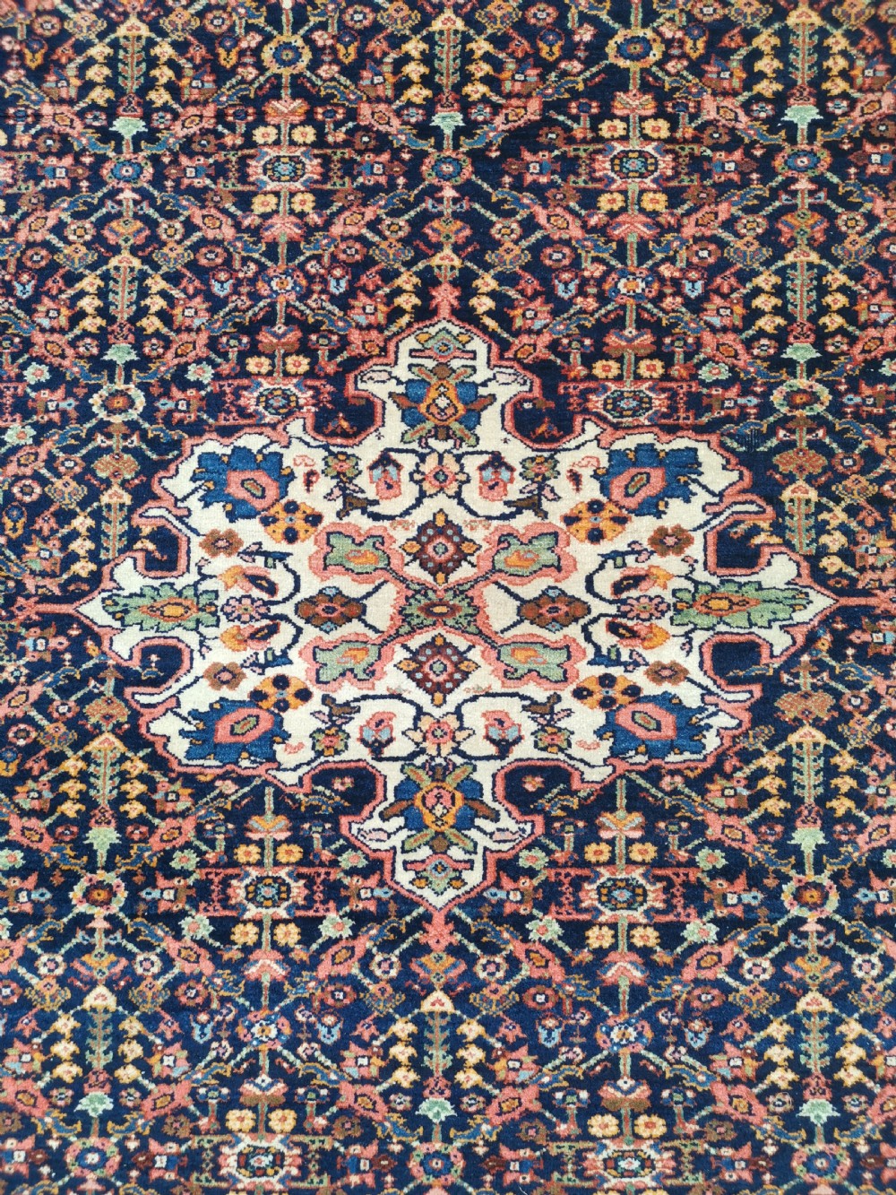 An antique hand-knotted Persian Jozan rug featuring a cream central medallion surrounded by dense floral patterns on a dark navy field with a red border. View II