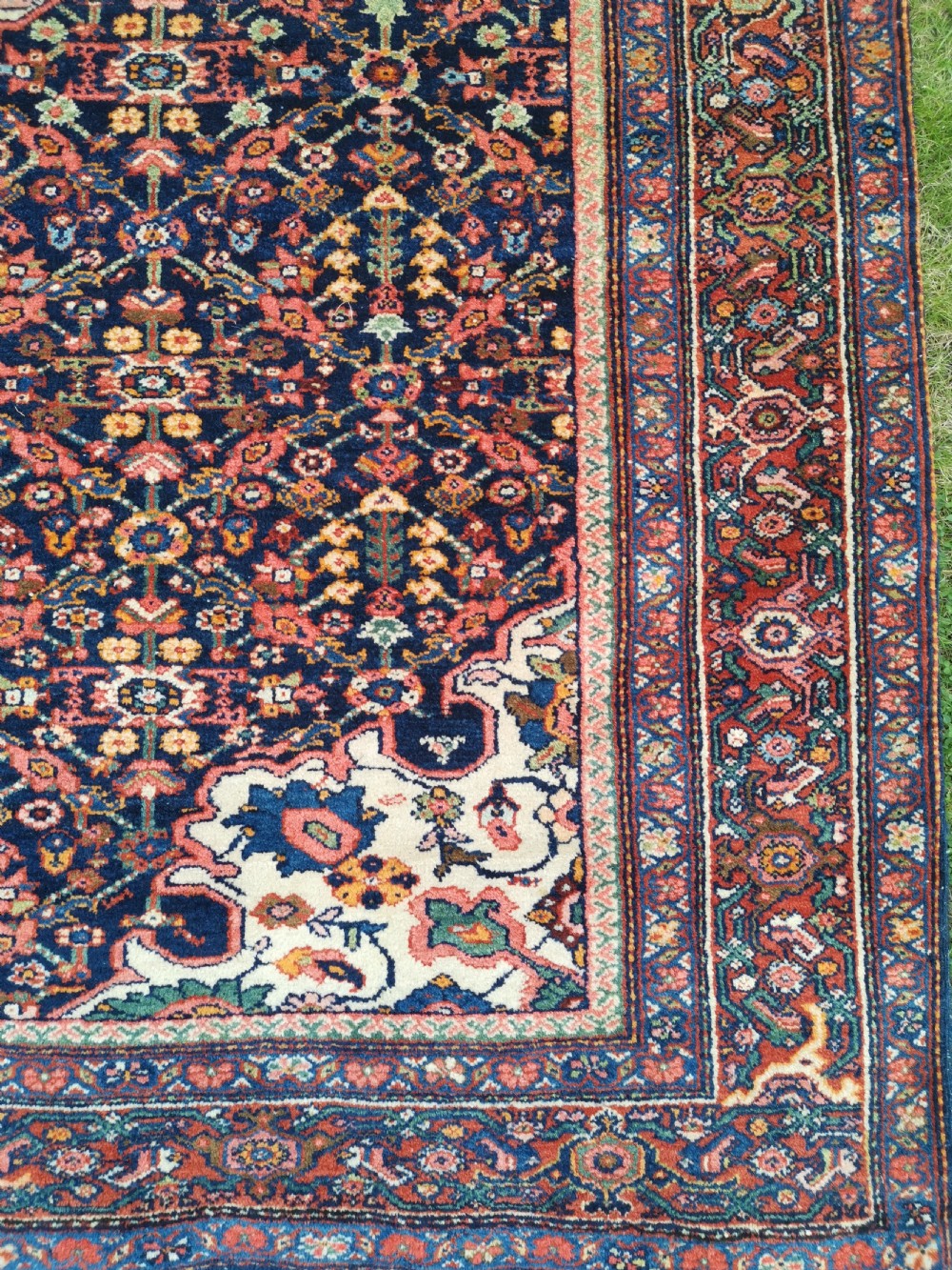 An antique hand-knotted Persian Jozan rug featuring a cream central medallion surrounded by dense floral patterns on a dark navy field with a red border. View III