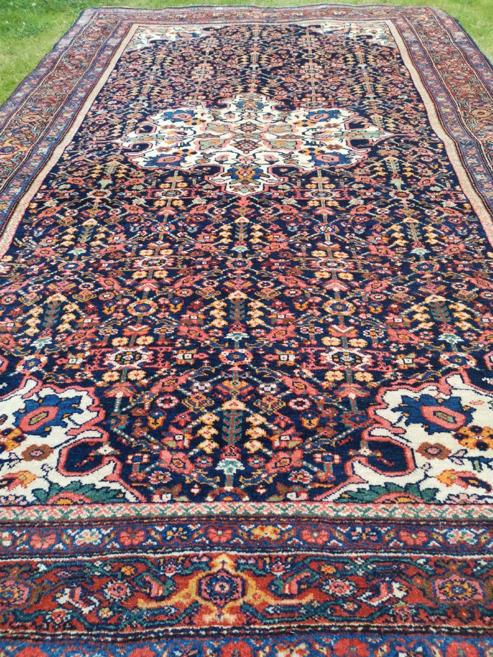 An antique hand-knotted Persian Jozan rug featuring a cream central medallion surrounded by dense floral patterns on a dark navy field with a red border. View VI