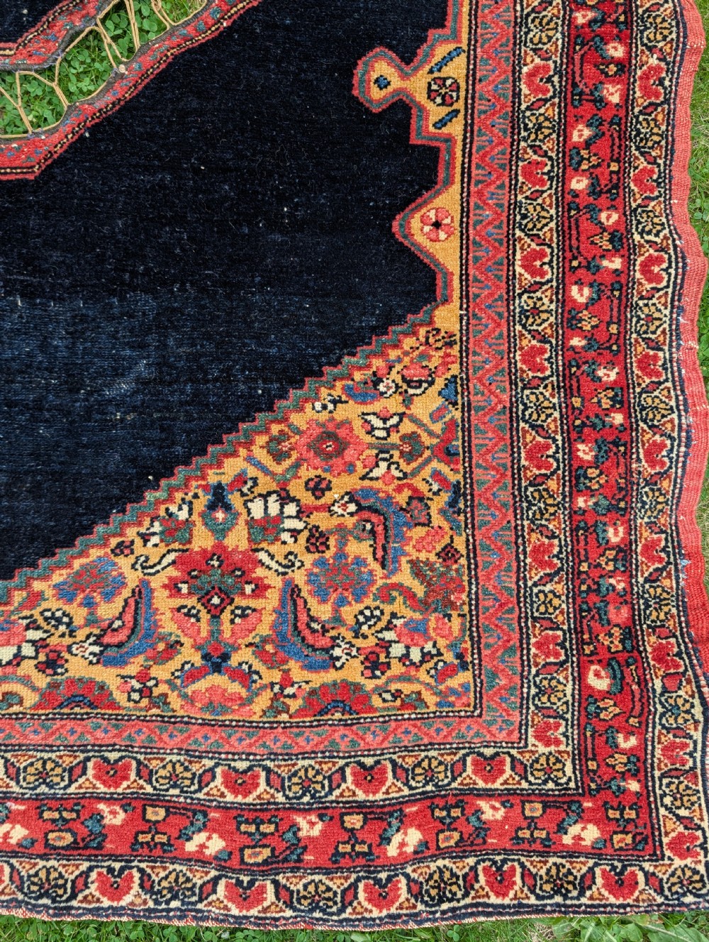 An antique hand-knotted Persian Senneh saddle cover featuring a dark navy field with a central saddle notch, floral spandrels, and multi-banded red patterned borders. View III